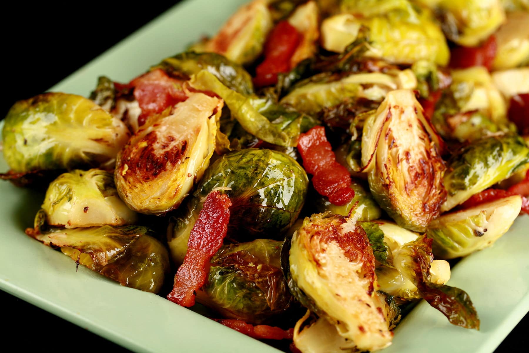 A pale green platter, mounded with roasted Brussels Sprouts. Chopped Bacon is visible throughout.