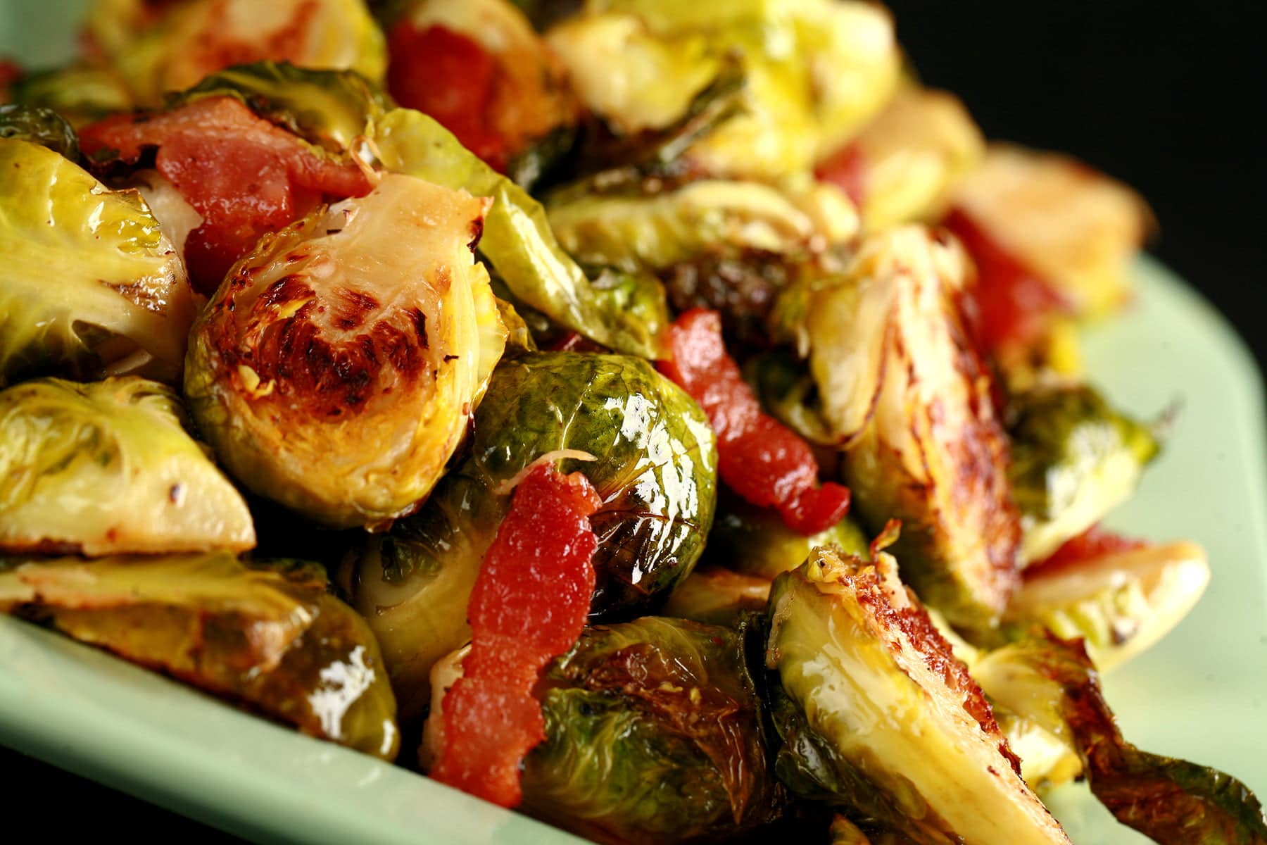 A pale green platter, mounded with roasted Brussels Sprouts. Chopped Bacon is visible throughout.