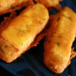 A close up view of several sticks of paneer pakora - Indian fried cheese sticks. Bits of cilantro are visible in the golden yellow batter.