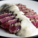 Pepper crusted tuna with wasabi cream sauce. The tuna steak has been cooked rare, sliced up, and fanned out on the plate before being topped with the sauce.