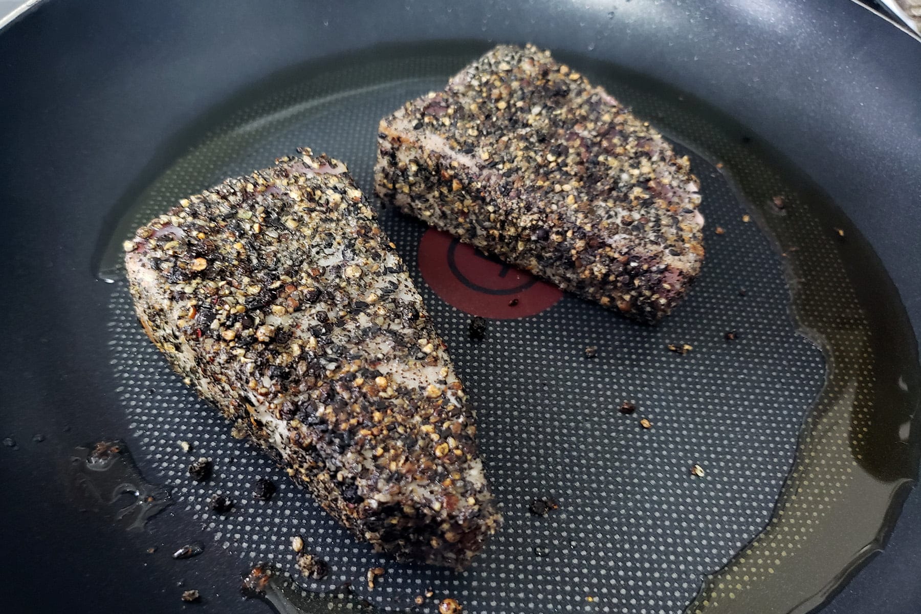2 Pepper crusted tuna steaks, cooking in a nonstick pan.