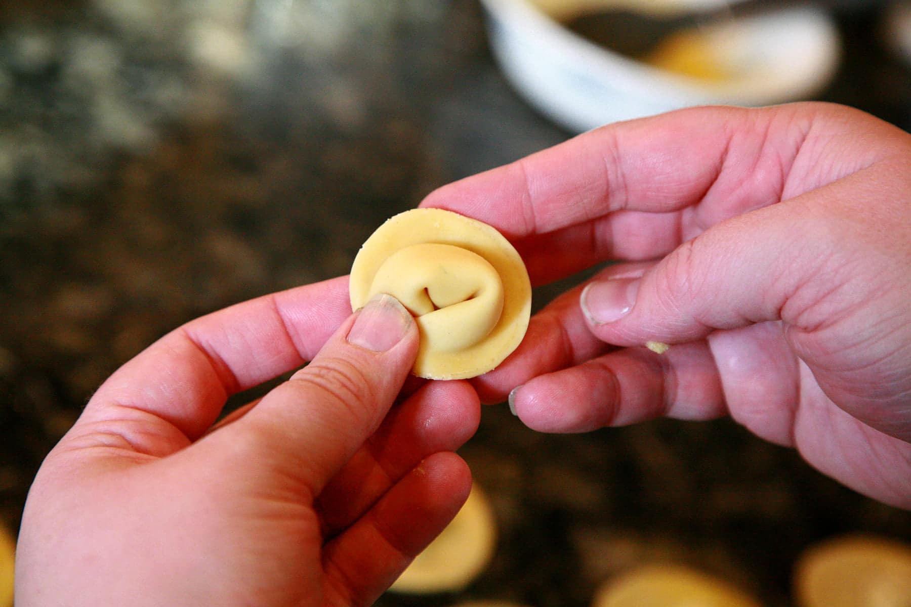 Two hands hold a recently folded tortellini.