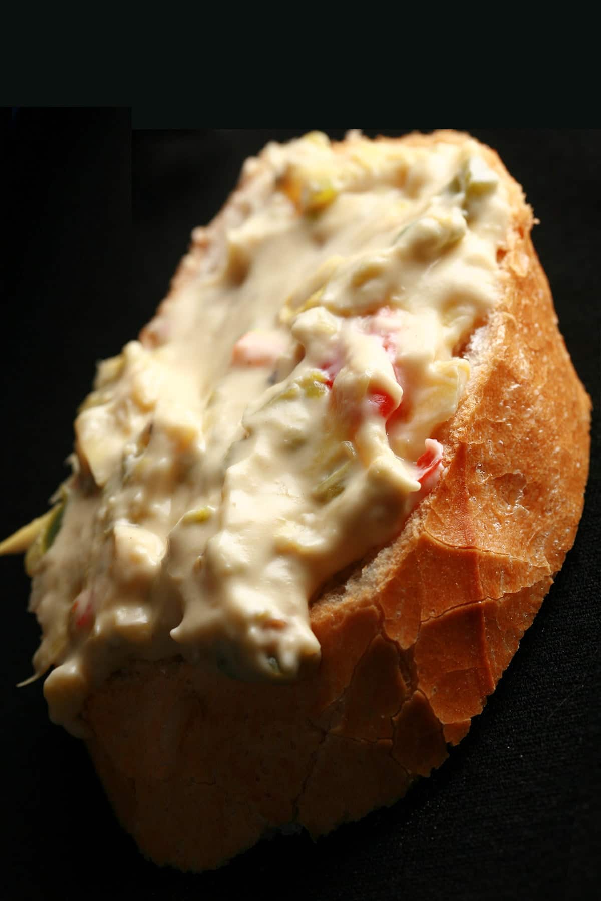 A slice of baguette spread with Backfire dip - a chunky jalapeno artichoke cheese dip.