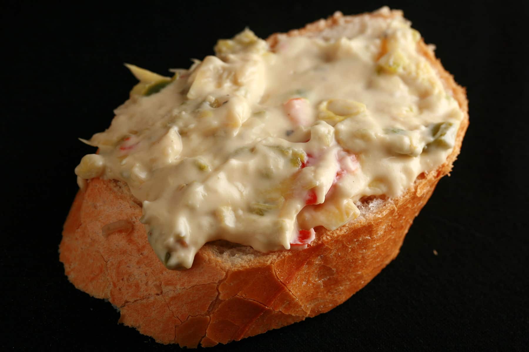 A slice of baguette spread with Backfire dip - a chunky jalapeno artichoke cheese dip.