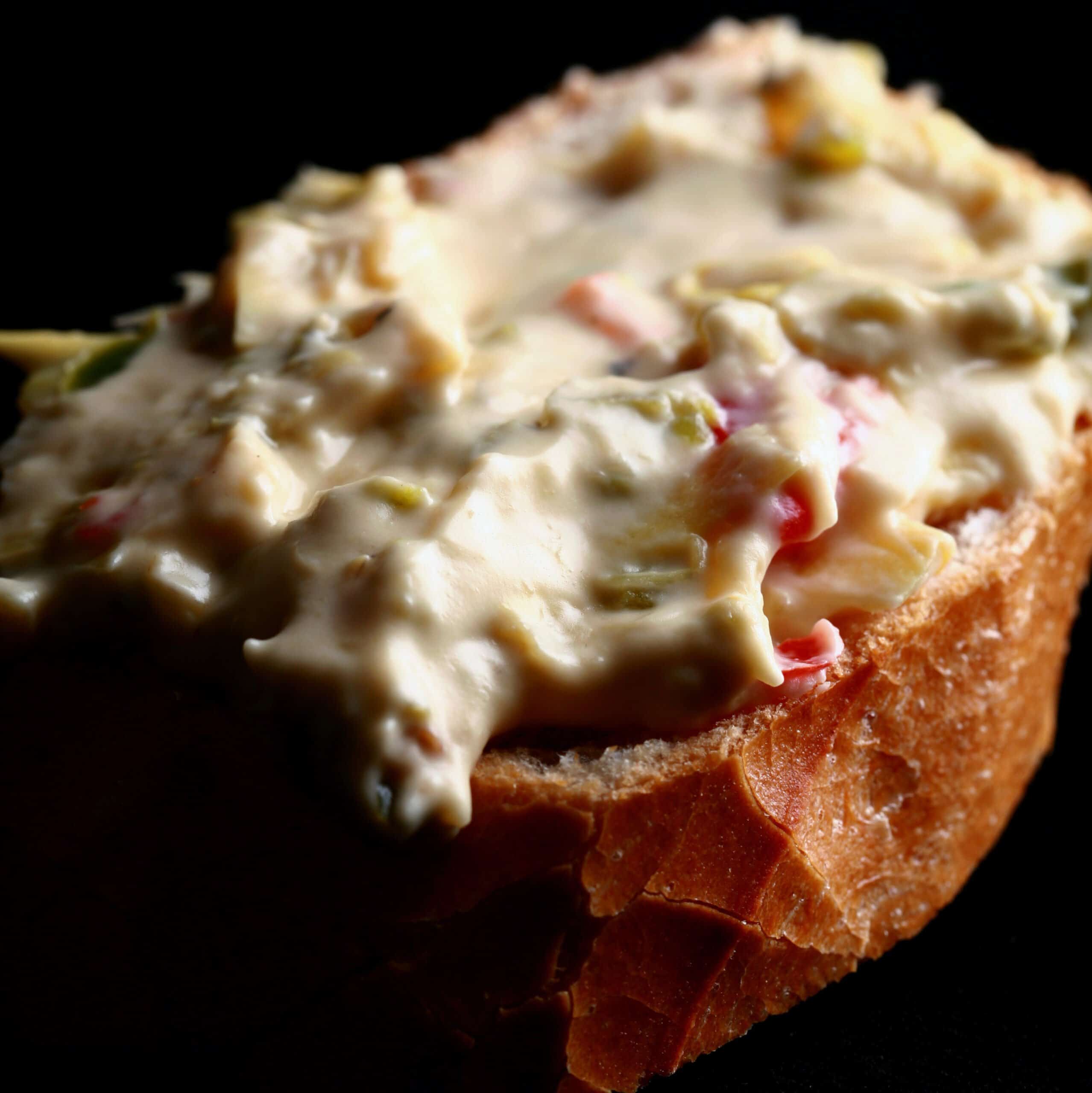 A slice of baguette spread with Backfire dip - a chunky jalapeno artichoke cheese dip.