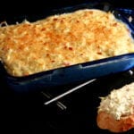 A small, blue, rectangular glass pan, filled with a golden brown cheese dip. In the foreground is a slice of baguette spread with the artichoke jalapeno cheese dip.