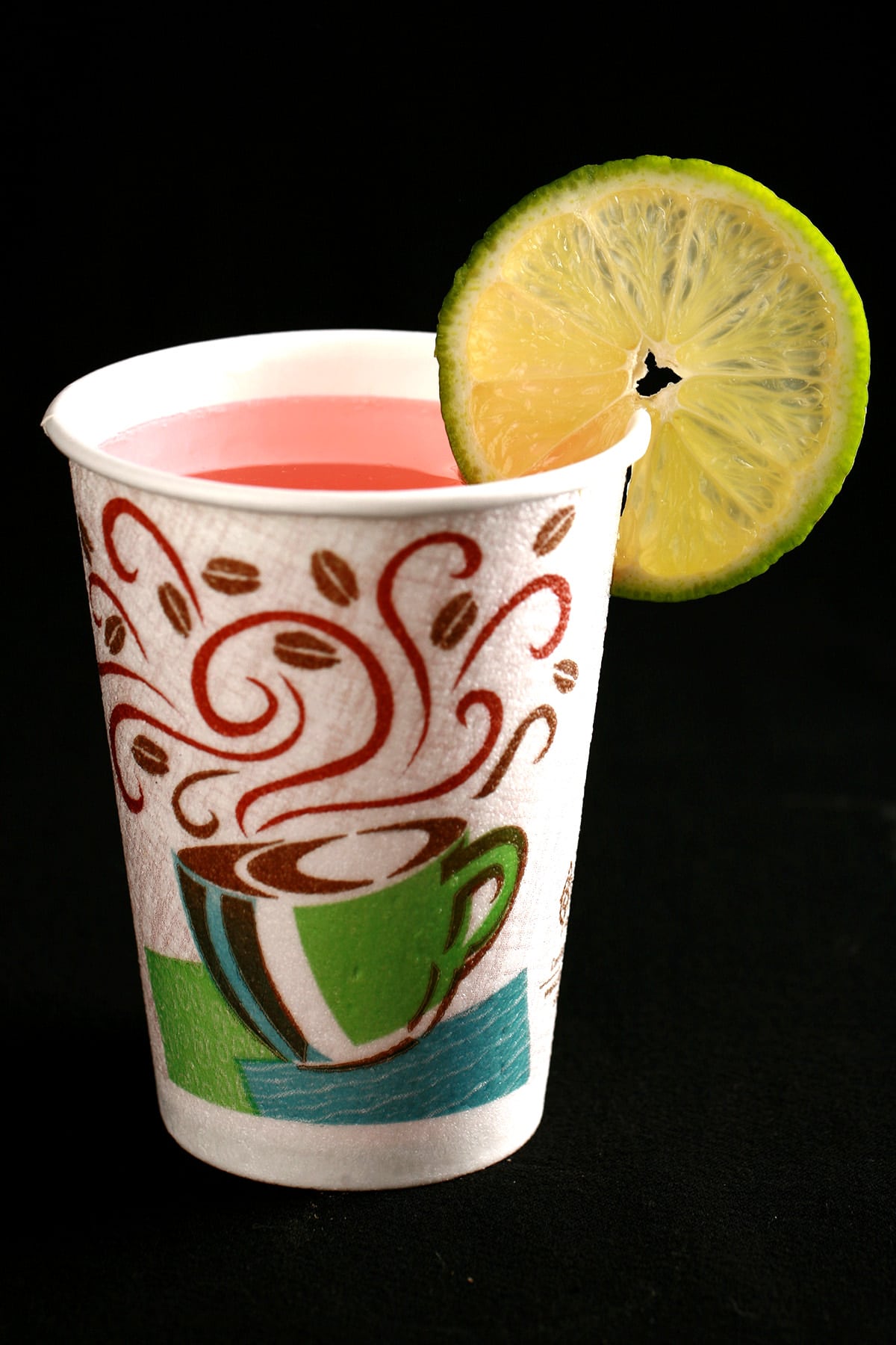 The Drinking In LA - a light pink fizzy cocktail in a hotel room disposable coffee cup. It is garnished with a slice of lime.