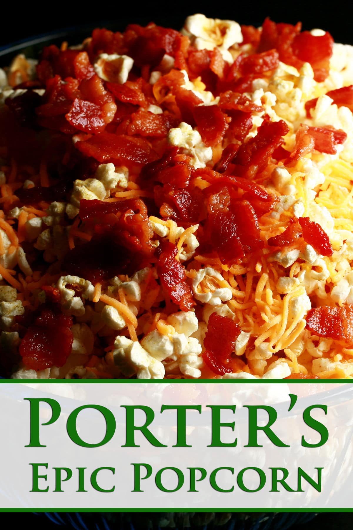 A close up view of popcorn with shredded cheddar cheese and crispy bacon on top.