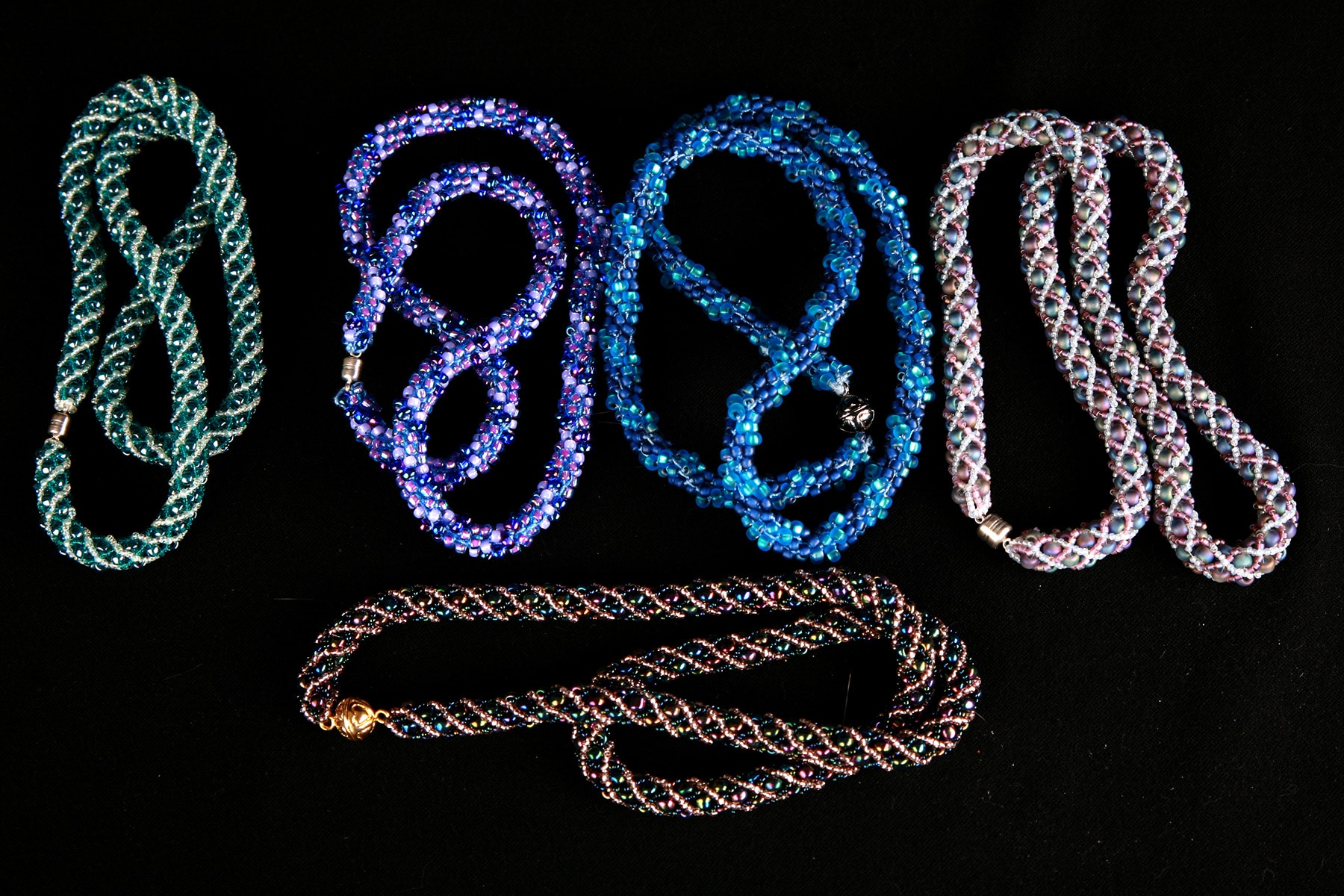 5 beaded necklaces on a black background.