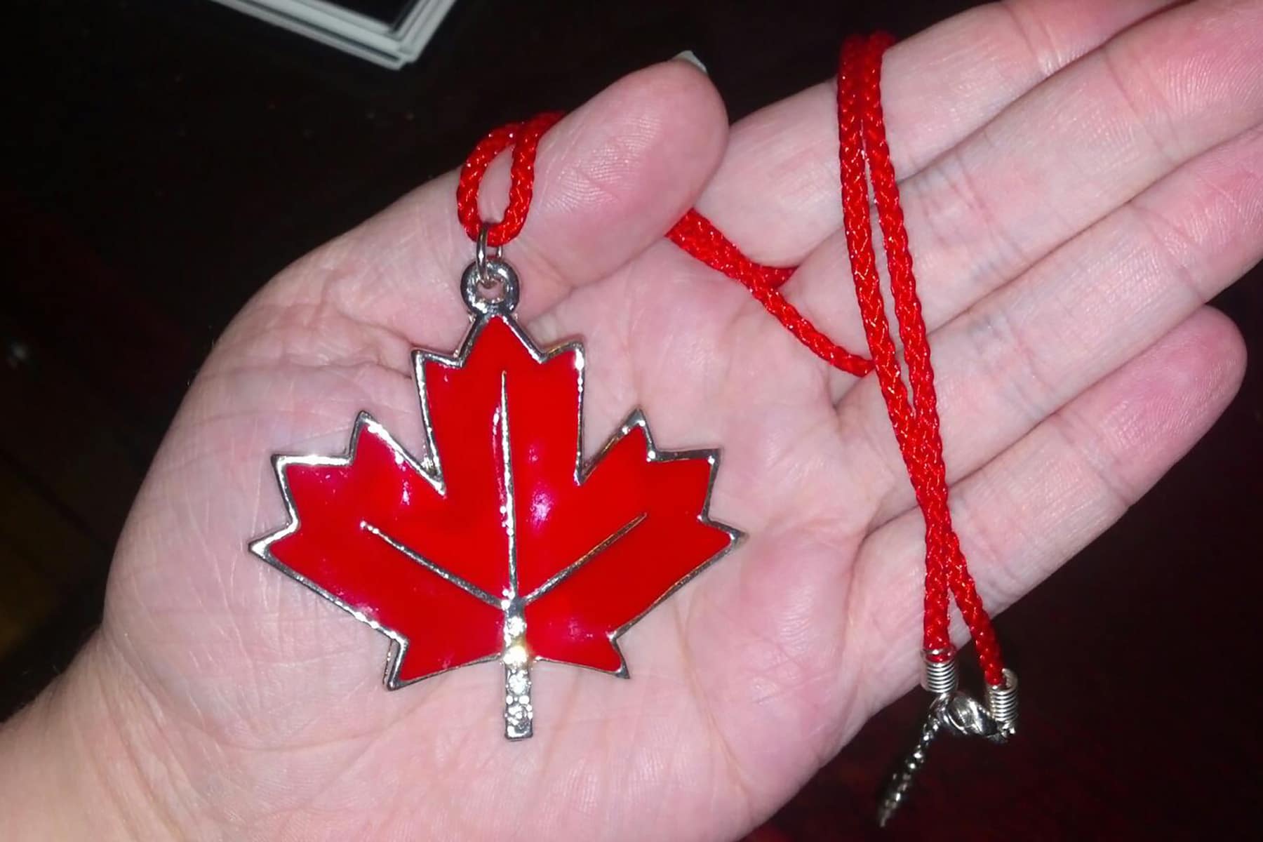 A hand holds a large red maple leaf pendant.