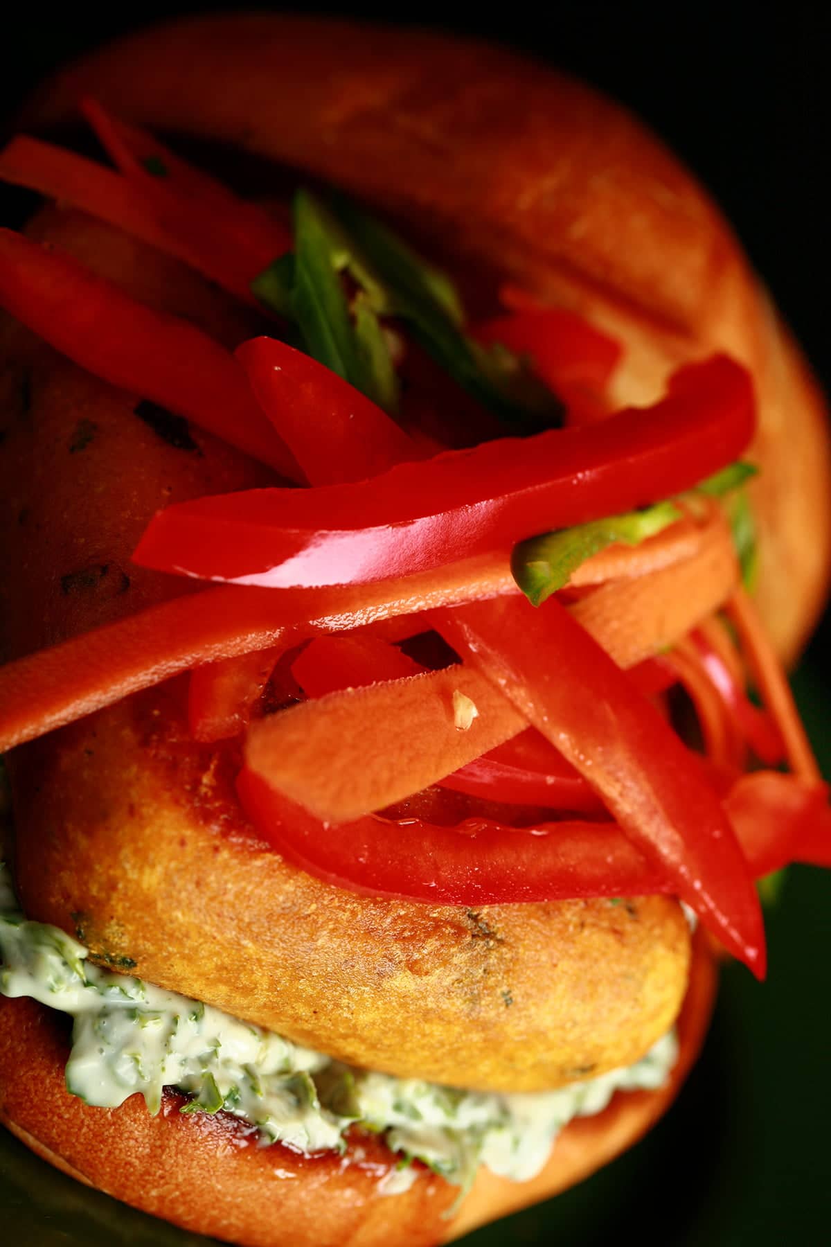 A very close up view of a Paneer Burger - a pakora battered patty of paneer, with cilantro-mint mayonnaise and a pickled slaw made of red peppers, carrots, and jalapenos, on a bun.