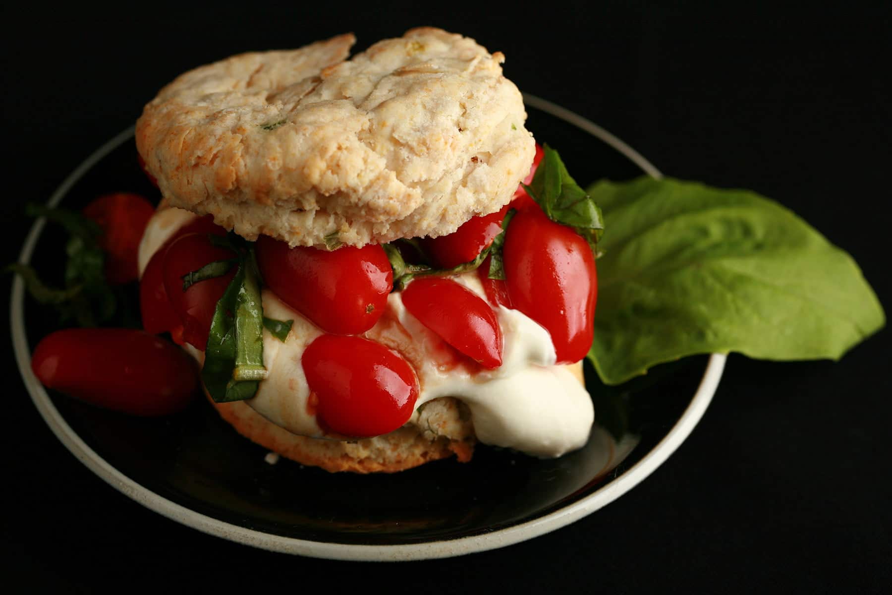 Savoury Tomato Shortcake: A baking powder biscuit "sandwich" on a small black plate.  The biscuit has soft white cheese, cherry tomatoes, and fresh basil as its filling.