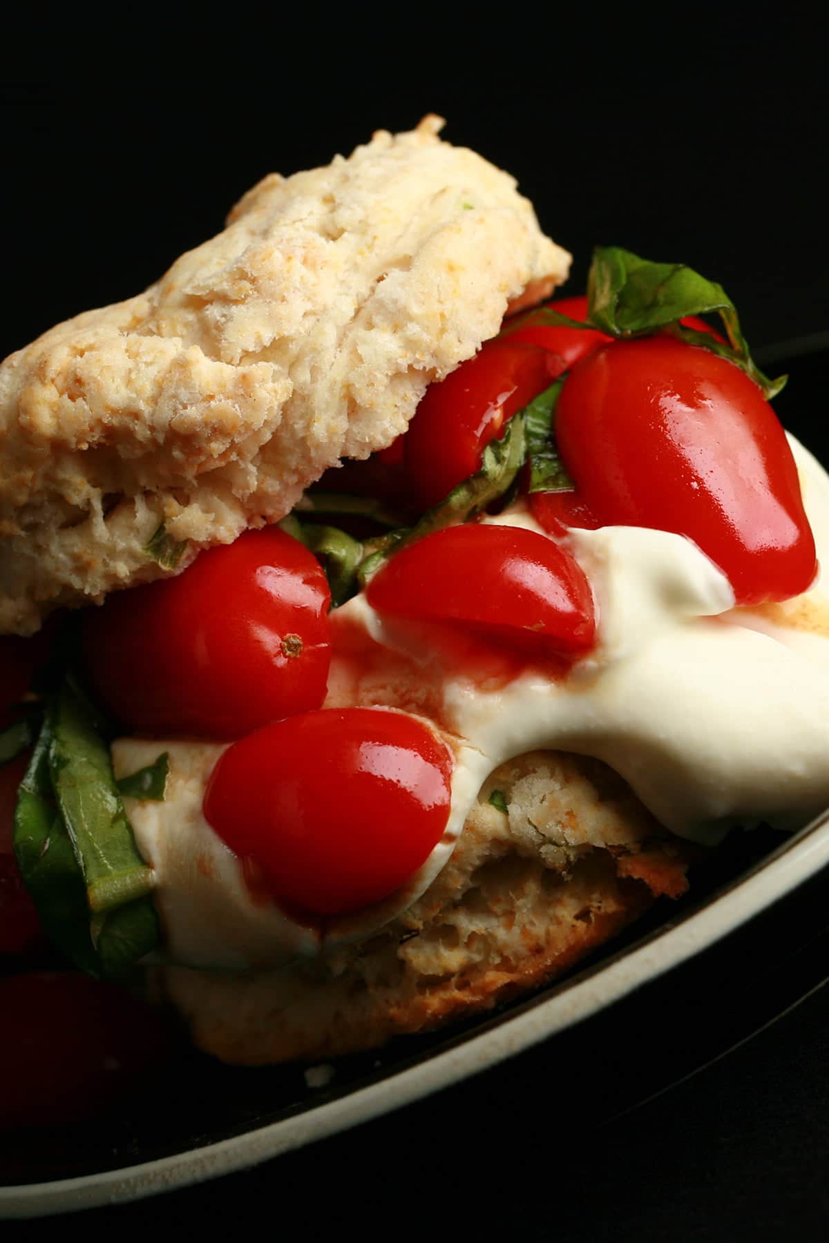 Savoury Tomato Shortcake: A baking powder biscuit "sandwich" on a small black plate.  The biscuit has soft white cheese, cherry tomatoes, and fresh basil as its filling.