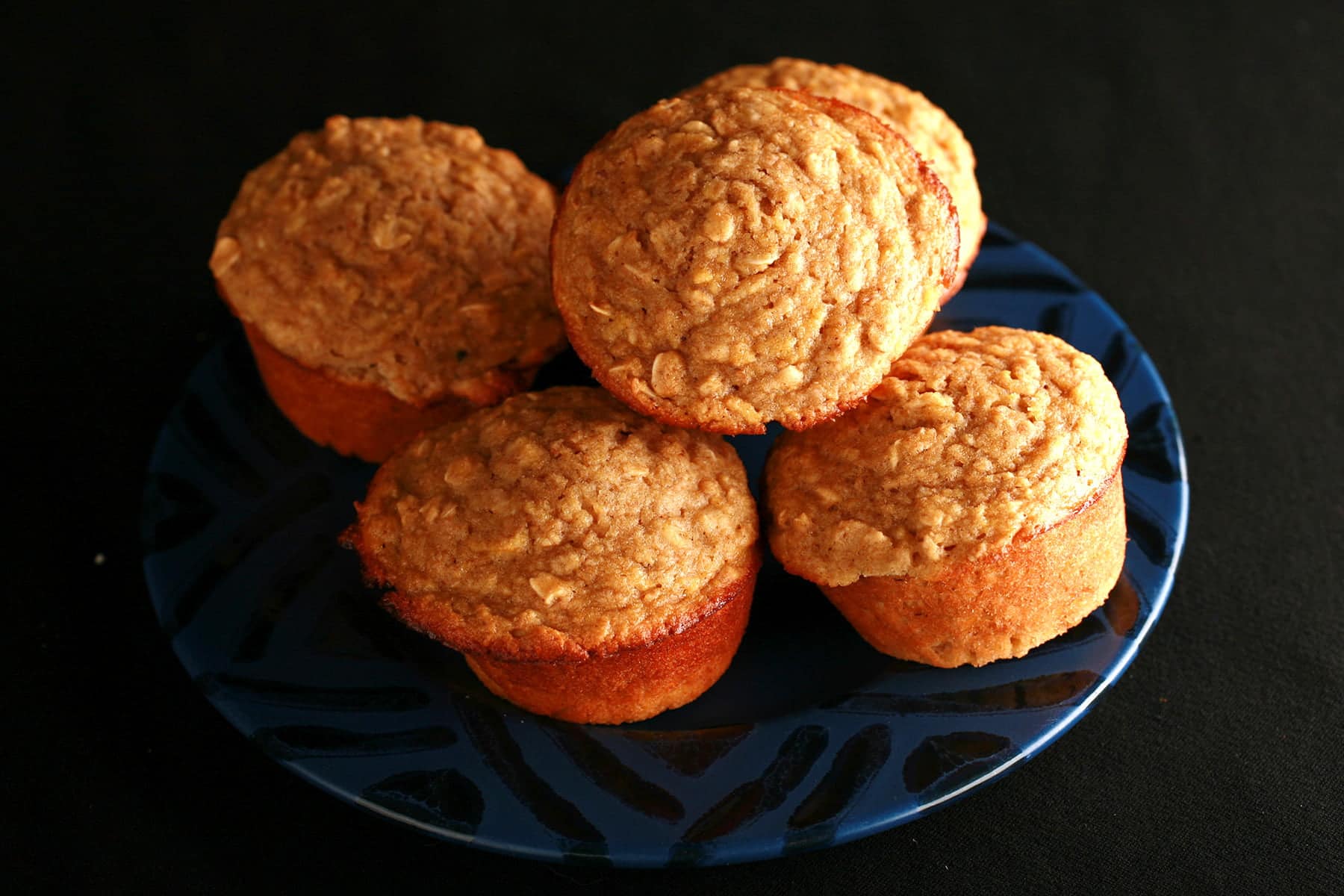 A small blue plate with a black geometric design around the edge is stacked with these healthier apple oatmeal muffins.