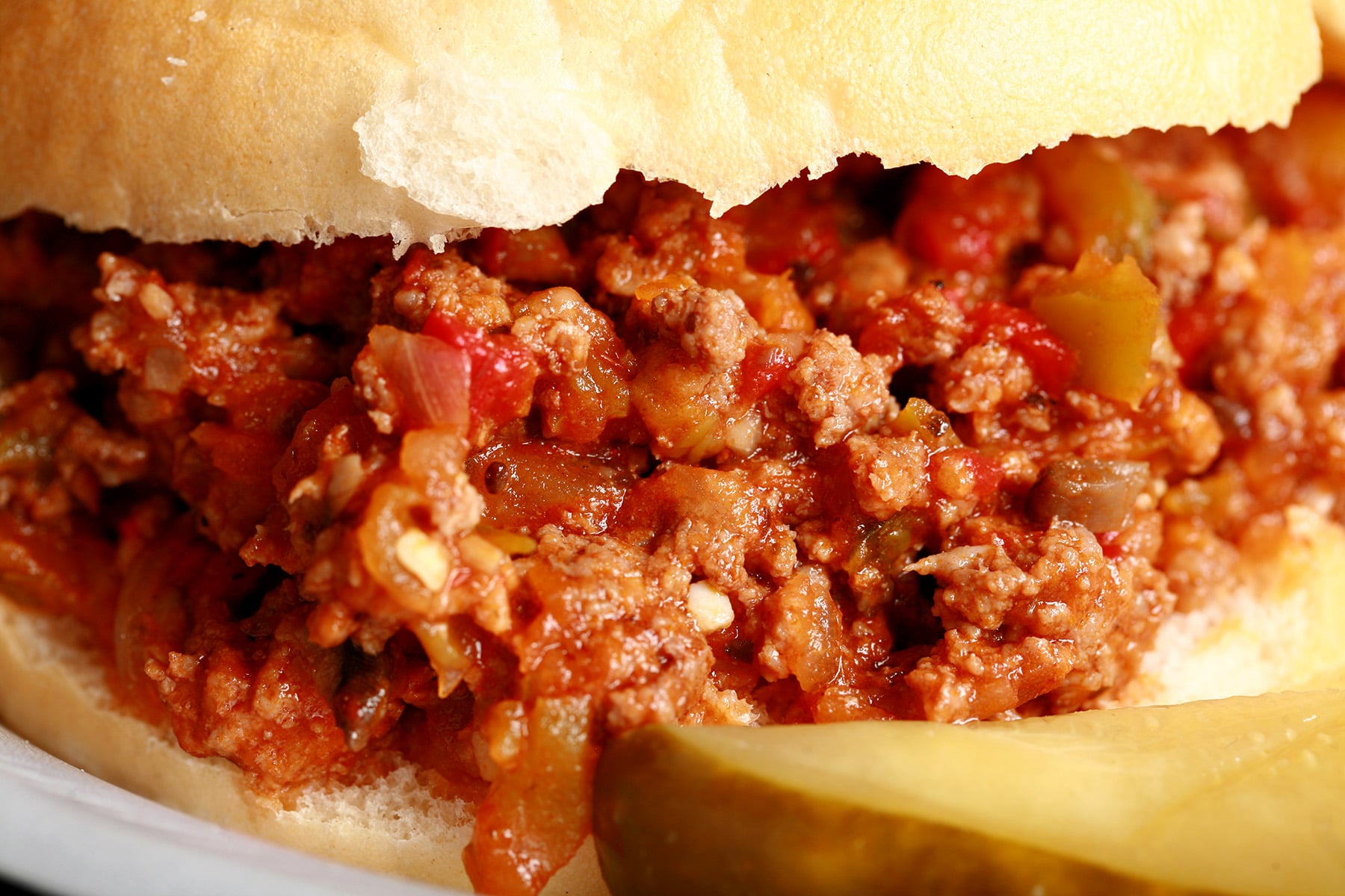 A Homemade Sloppy Joes sandwich on a paper plate, with chips and a pickle spear.