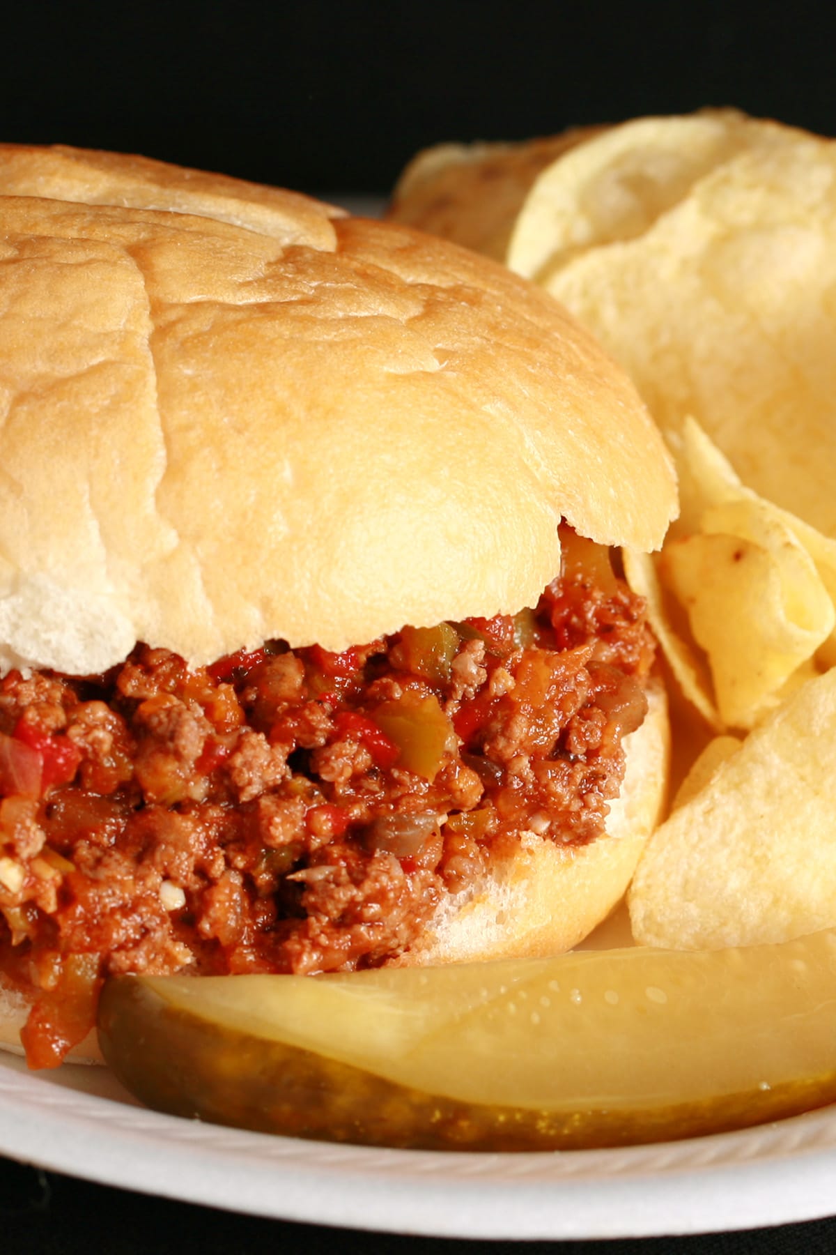 A Convention Sloppy Joes sandwich on a paper plate, with chips and a pickle spear.
