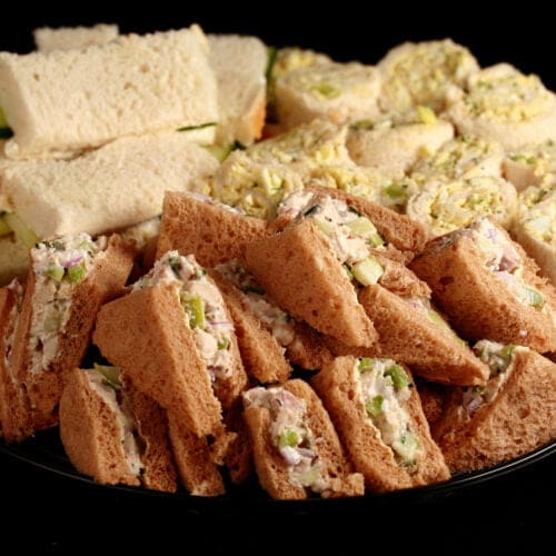 A large platter of fancy tea sandwiches. Cucumber cream cheese finger sandwiches, egg salad pinwheels, and tarragon chicken salad triangles.