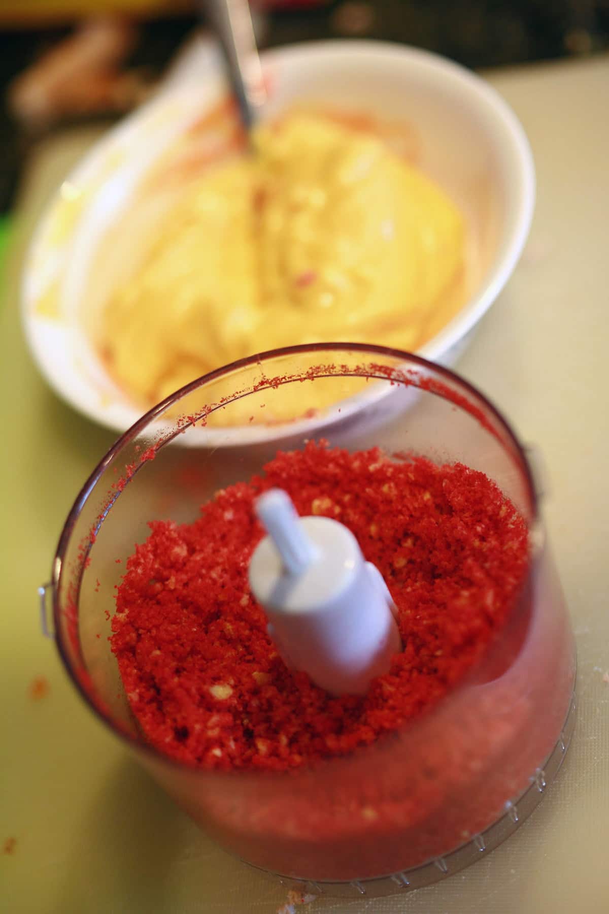 A bowl of Cheez Whiz nexy to a small foodprocessor with Hot Cheetos crumbs in it.