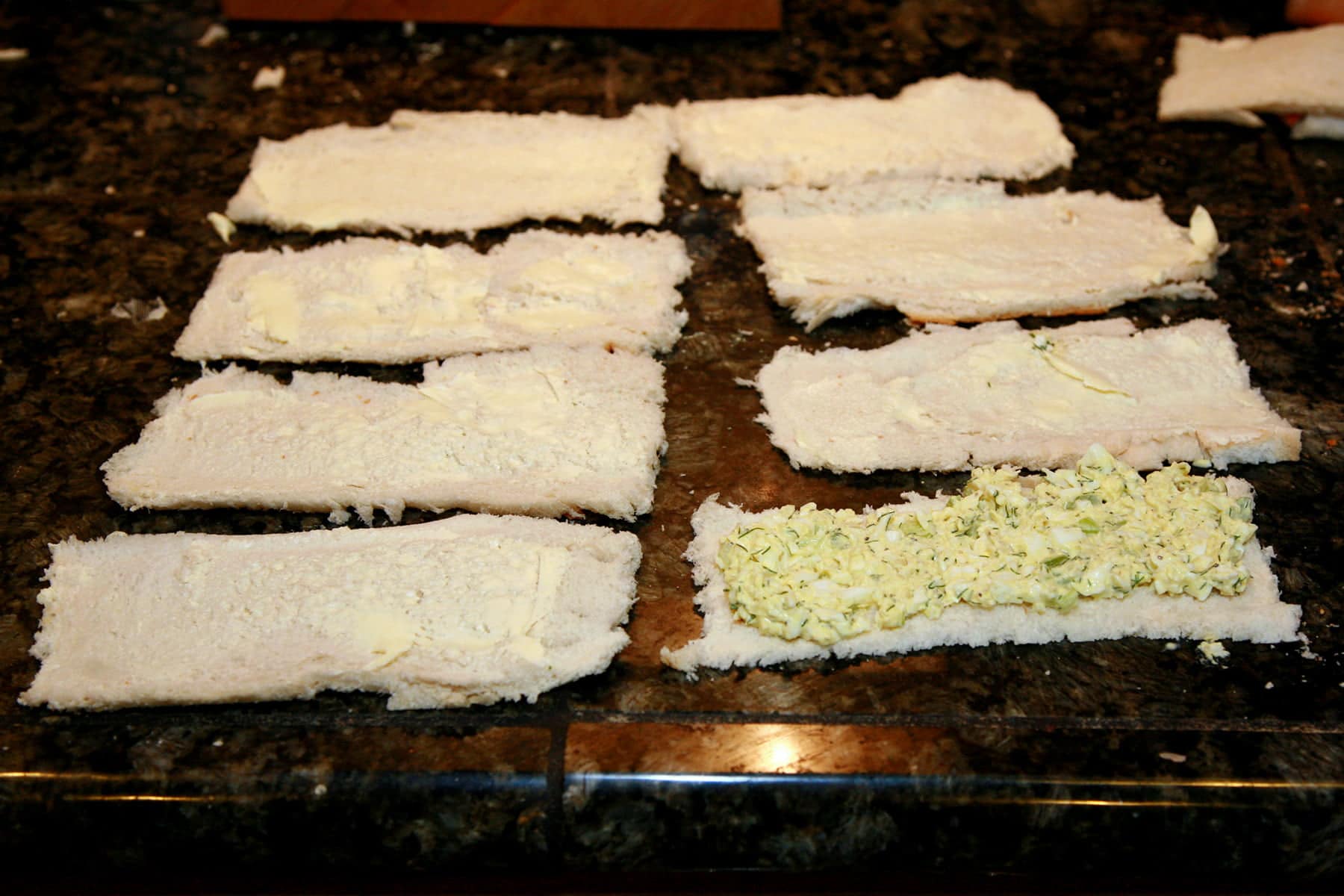 4 long slices of bread laid out on a counter, one with egg salad spread on it.