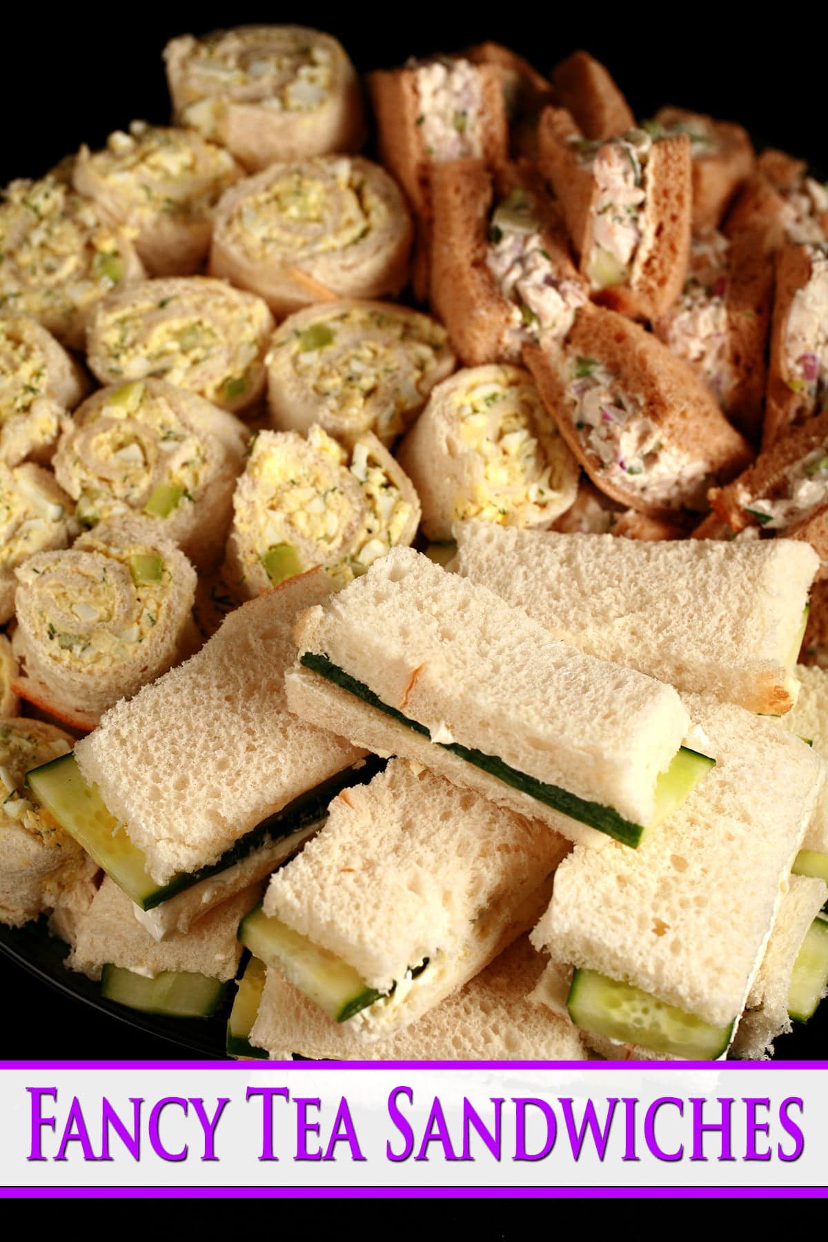 A large platter of fancy tea sandwiches. Cucumber cream cheese finger sandwiches, egg salad pinwheels, and tarragon chicken salad triangles.