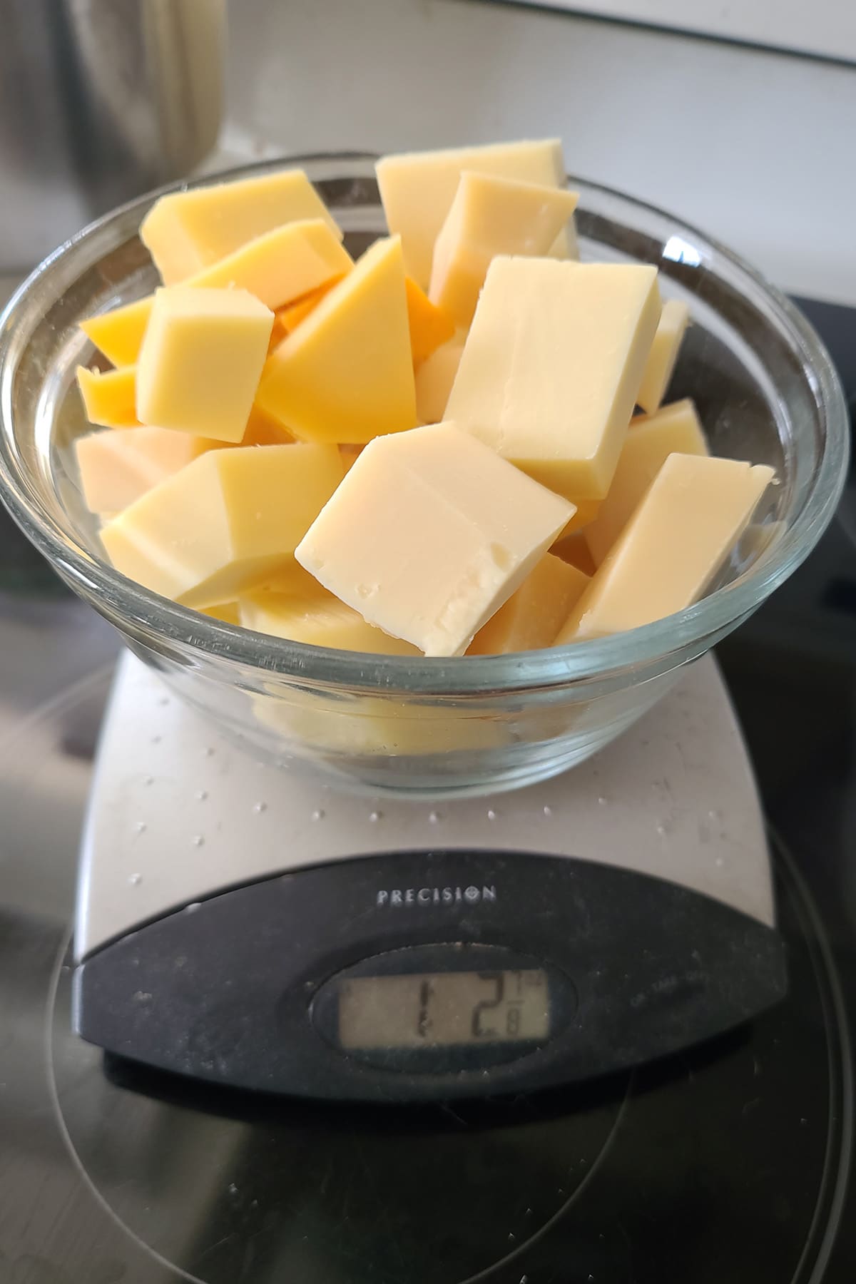 A glass bowl of cheese chunks on a scale. The scale reads 1 lb 2 oz.
