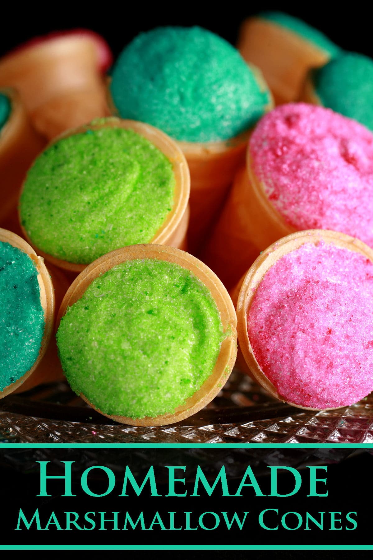 A pile of marshmallow cones - mini ice cream cones filled with marshmallow - are arranged on a plate. The exposed marshmallow of each is coated in colourful sugar - hot pink, lime green, and teal.