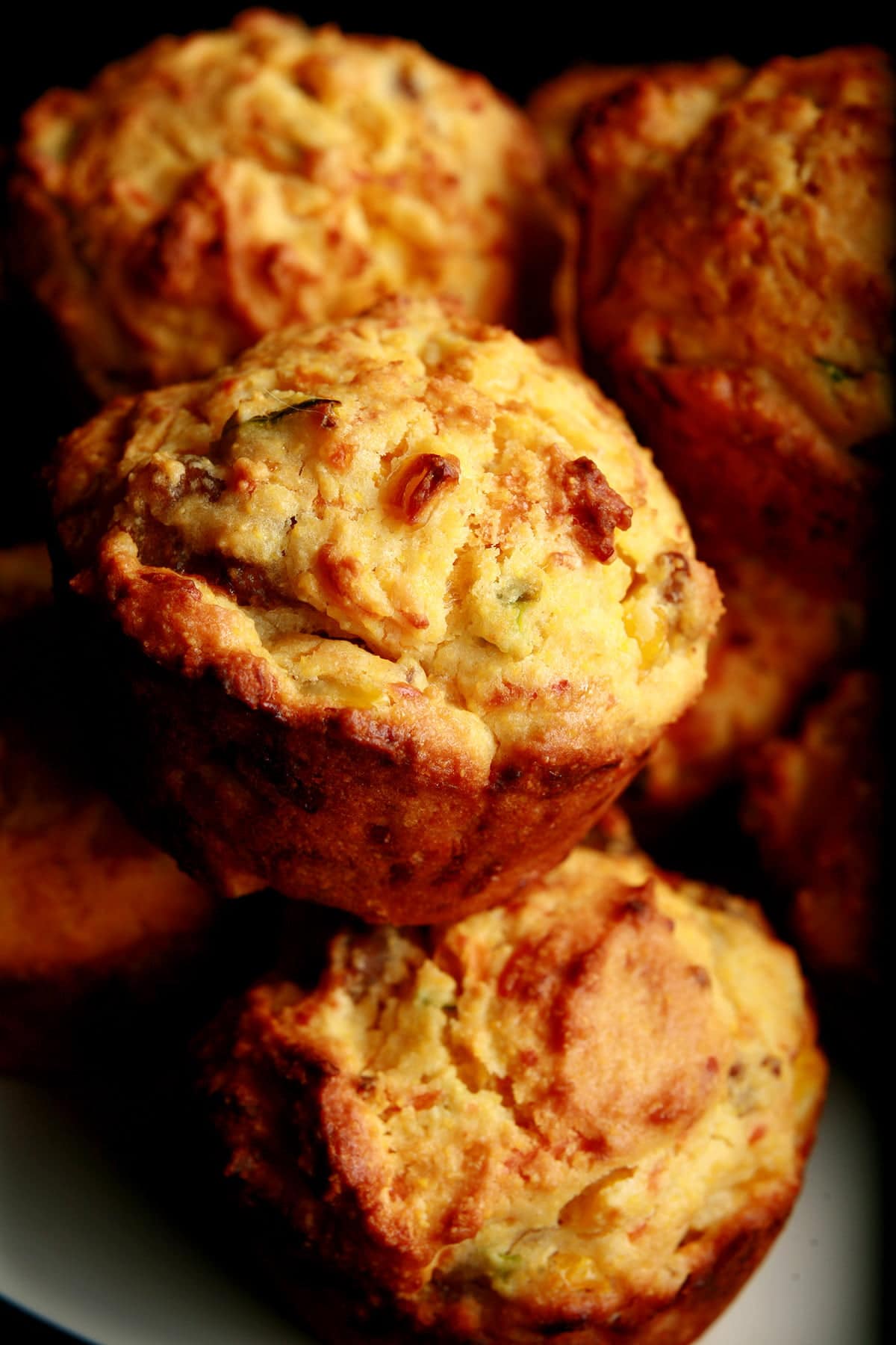A white plate stacked with a pile of breakfast corn muffins. Bits of cheese and green onion are visible in the muffins.