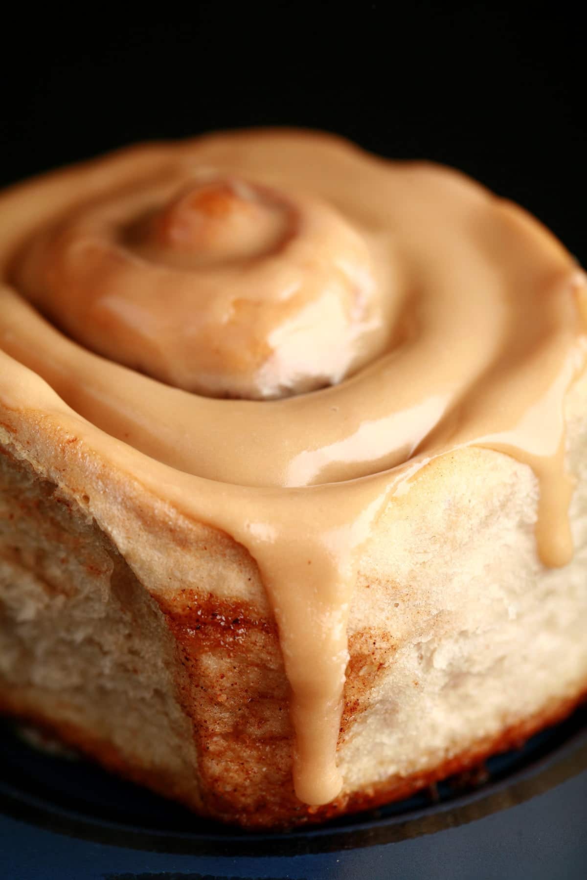 A close up view of a chai cinnamon roll, glazed with a light tan, tea flavoured frosting.