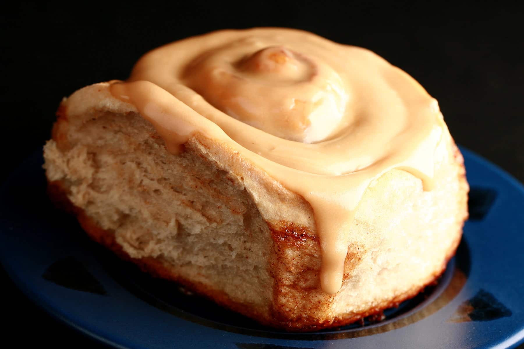 A close up view of a chai cinnamon roll, glazed with a light tan, tea flavoured frosting.