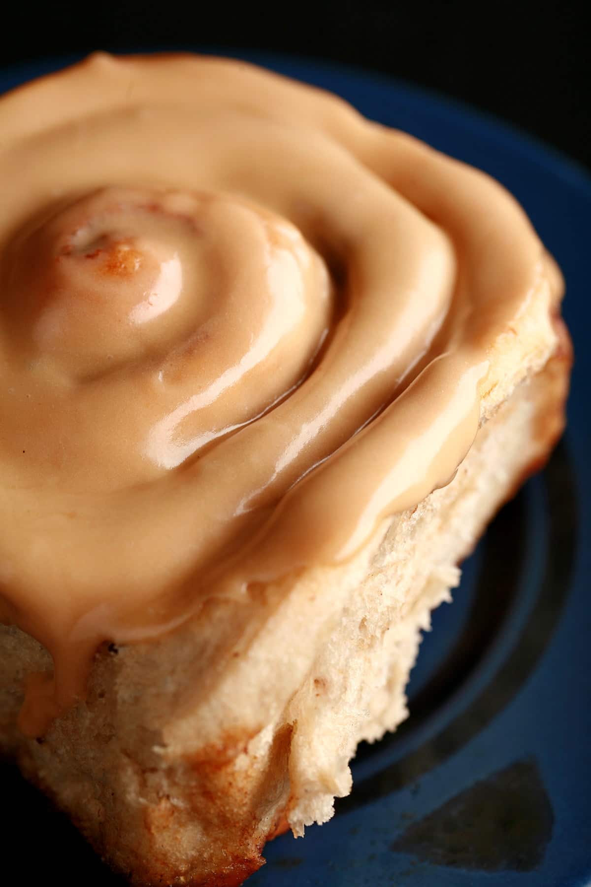 A close up view of a chai cinnamon bun, glazed with a light tan, tea flavoured frosting.
