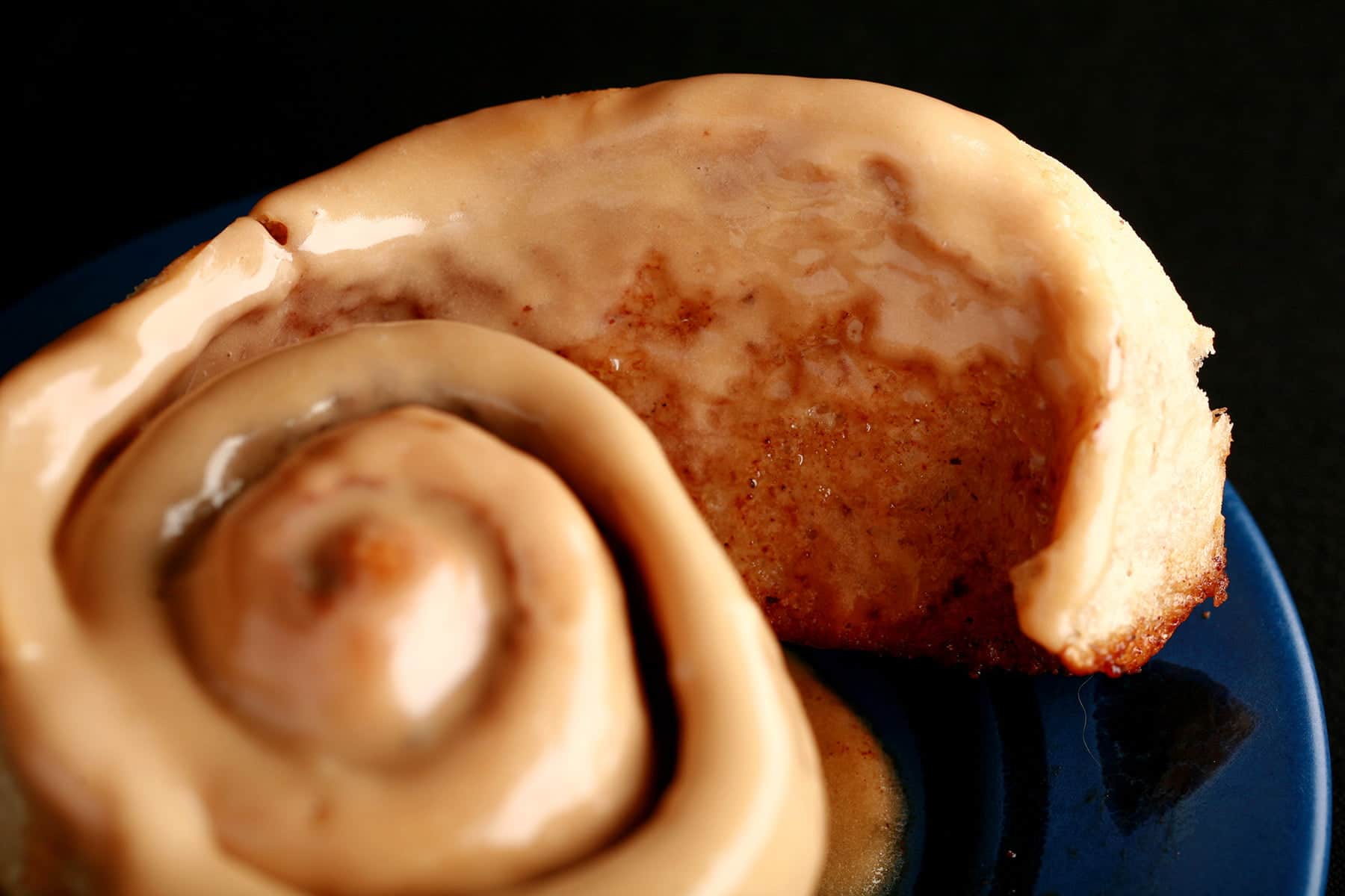 A close up view of a chai cinnamon bun, glazed with a light tan, tea flavoured frosting.