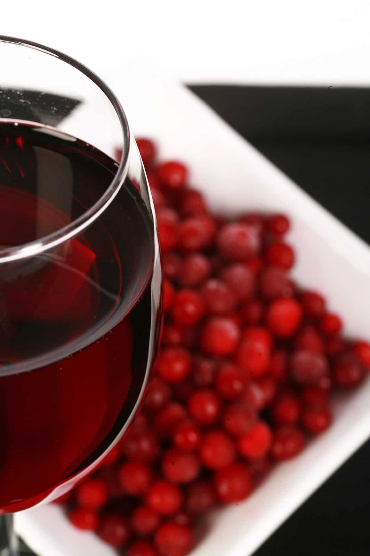 A glass of red wine - made from this lingonberry wine recipe - is pictured next to a small bowl of lingonberries.