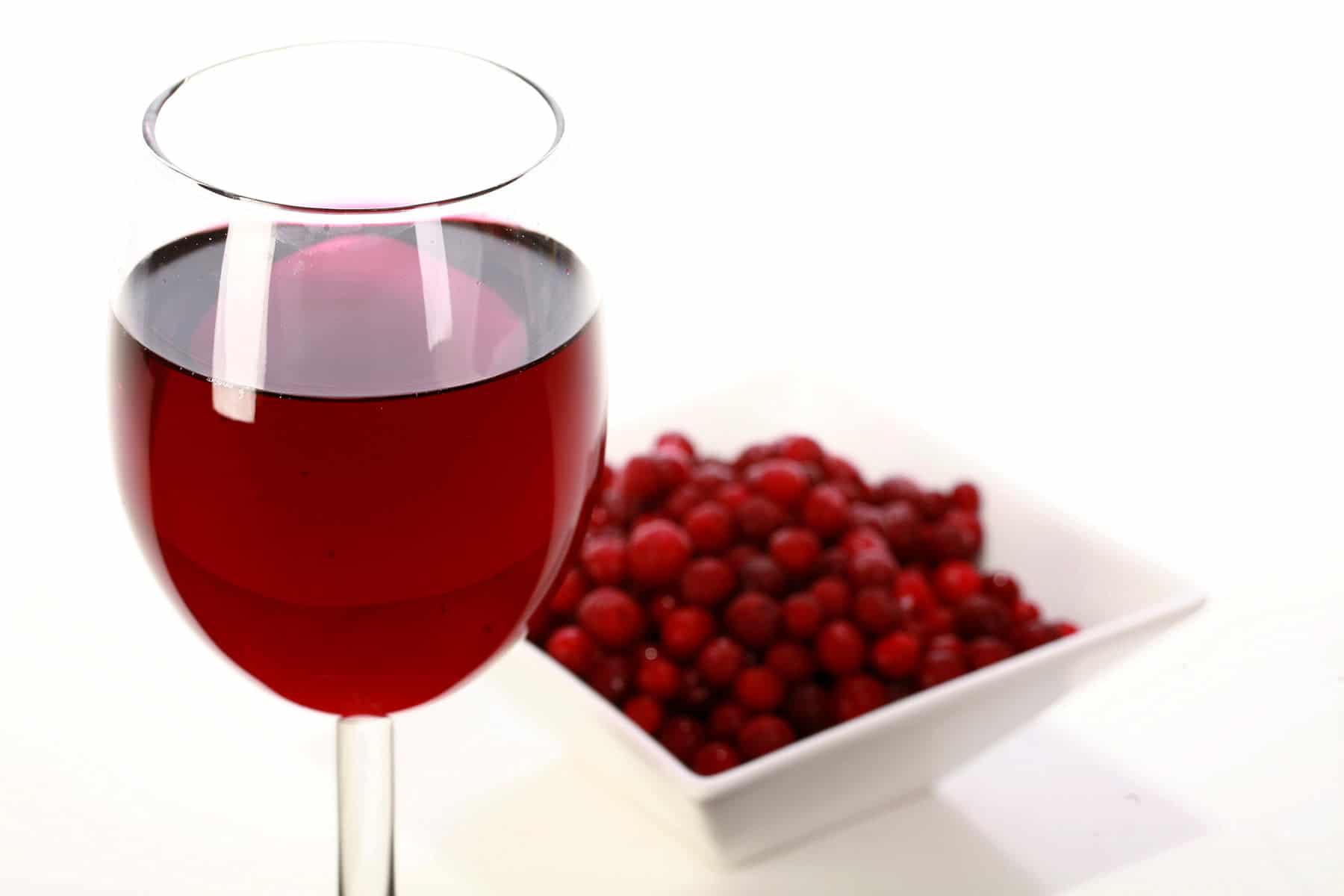A glass of red wine - made from this partridgeberry wine recipe - is pictured next to a small bowl of partridgeberries.