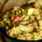 A plate of corn chips is shown with a bowl of chunky guacamole.