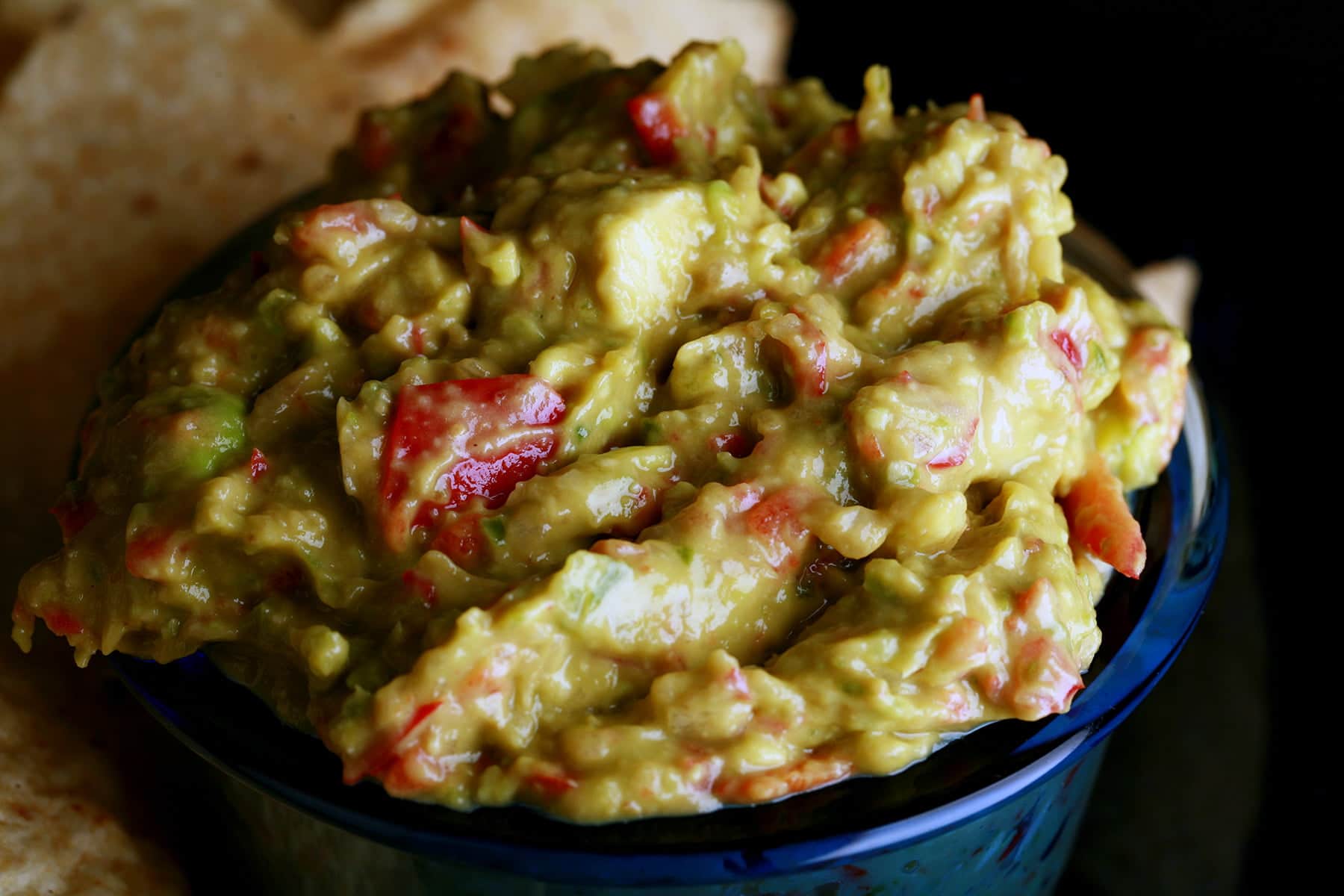 A plate of corn chips is shown with a bowl of chunky guacamole.