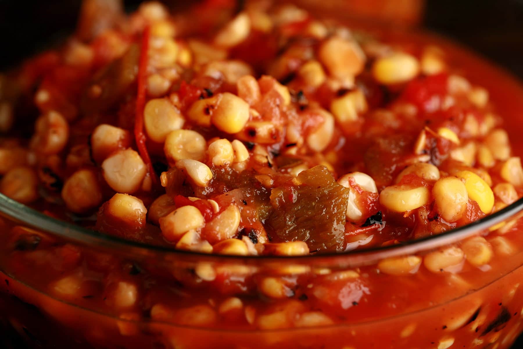 A close up view of roasted corn salsa for canning - corn salsa with tomatoes and peppers - in a glass bowl.