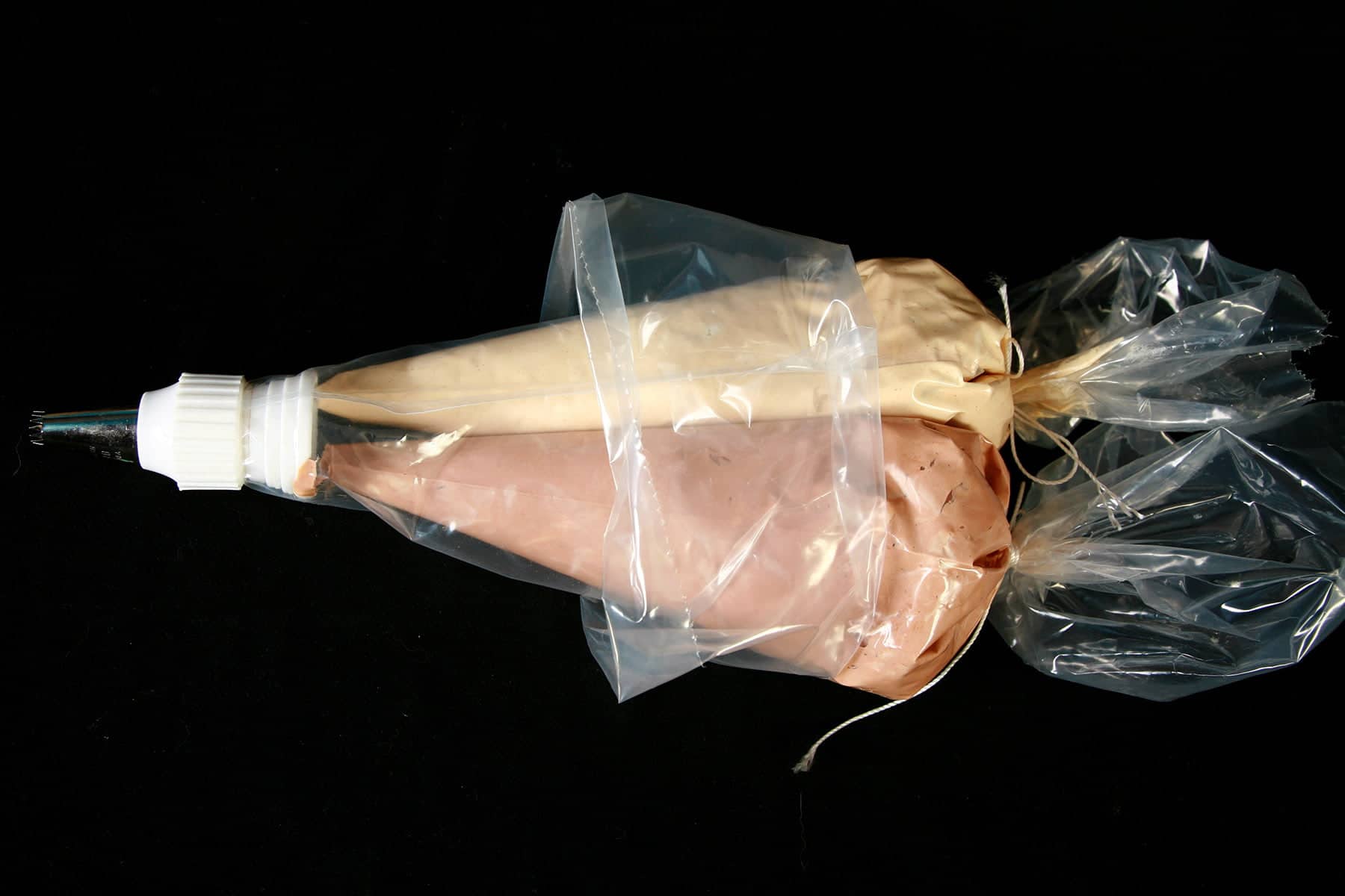 Two pastry bags filled with frosting - one tan, one brown - are shown inserted into a larger pastry bag that has been set up with a coupler and star tip.