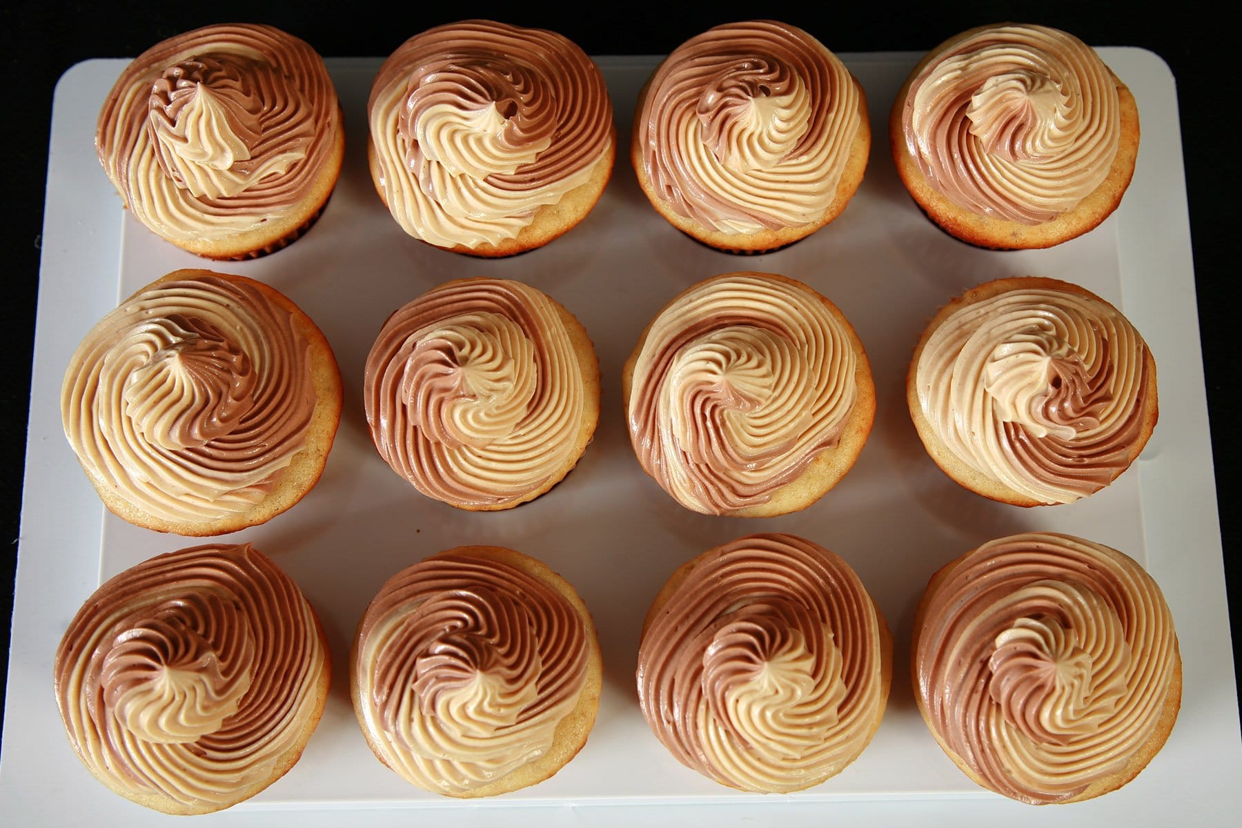 A tray of Fat Elvis Cupcakes - Banana cupcakes frosted with a two-tone swirl of Swiss Meringue buttercream, in both peanut butter and chocolate flavours.