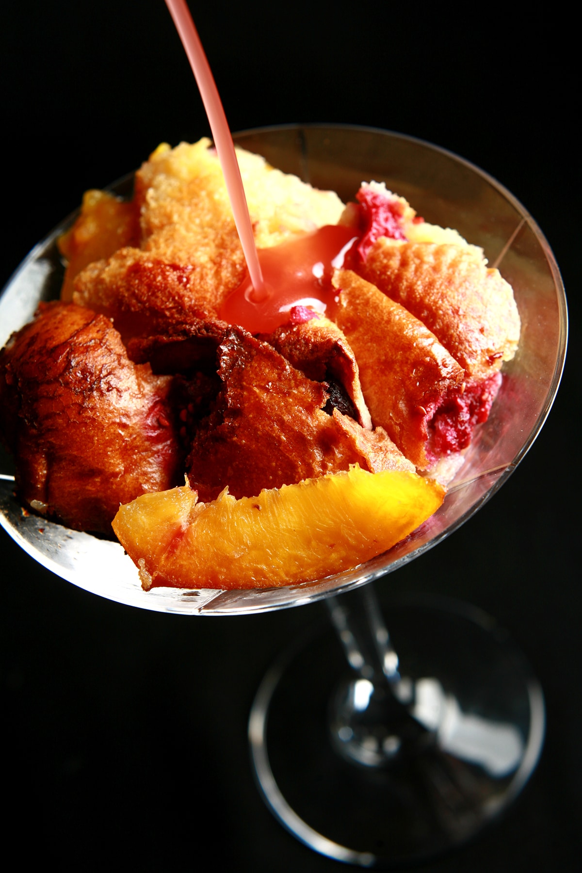 A serving of bread pudding in a martini glass. Peaches, raspberries, and a pink chambord sauce are visible.