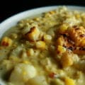 A white and cornflower blue bowl full of roasted corn chowder. Pieces of roasted corn garnish the surface of the soup.