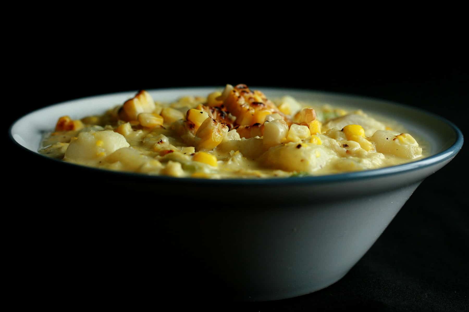 A white and cornflower blue bowl full of roasted corn chowder. Pieces of roasted corn garnish the surface of the soup.