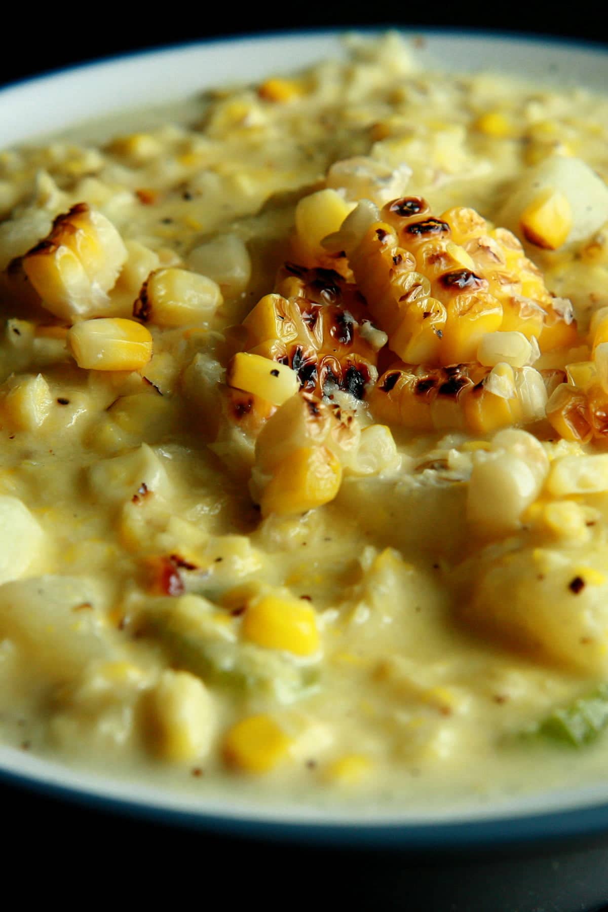 A white and cornflower blue bowl full of roasted corn chowder. Pieces of roasted corn garnish the surface of the soup.