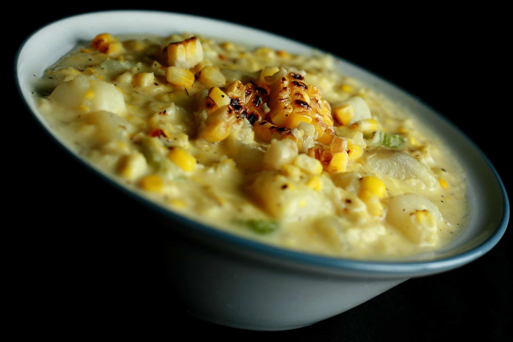 A white and cornflower blue bowl full of roasted corn chowder. Pieces of roasted corn garnish the surface of the soup.