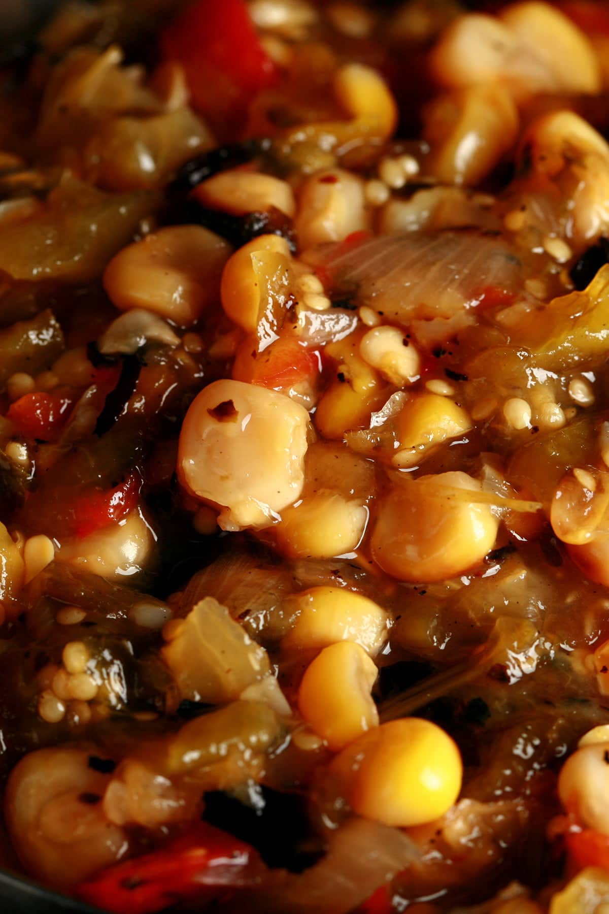 A close up view of a chunky roasted corn salsa verde - a green salsa with yellow corn and red peppers throughout.