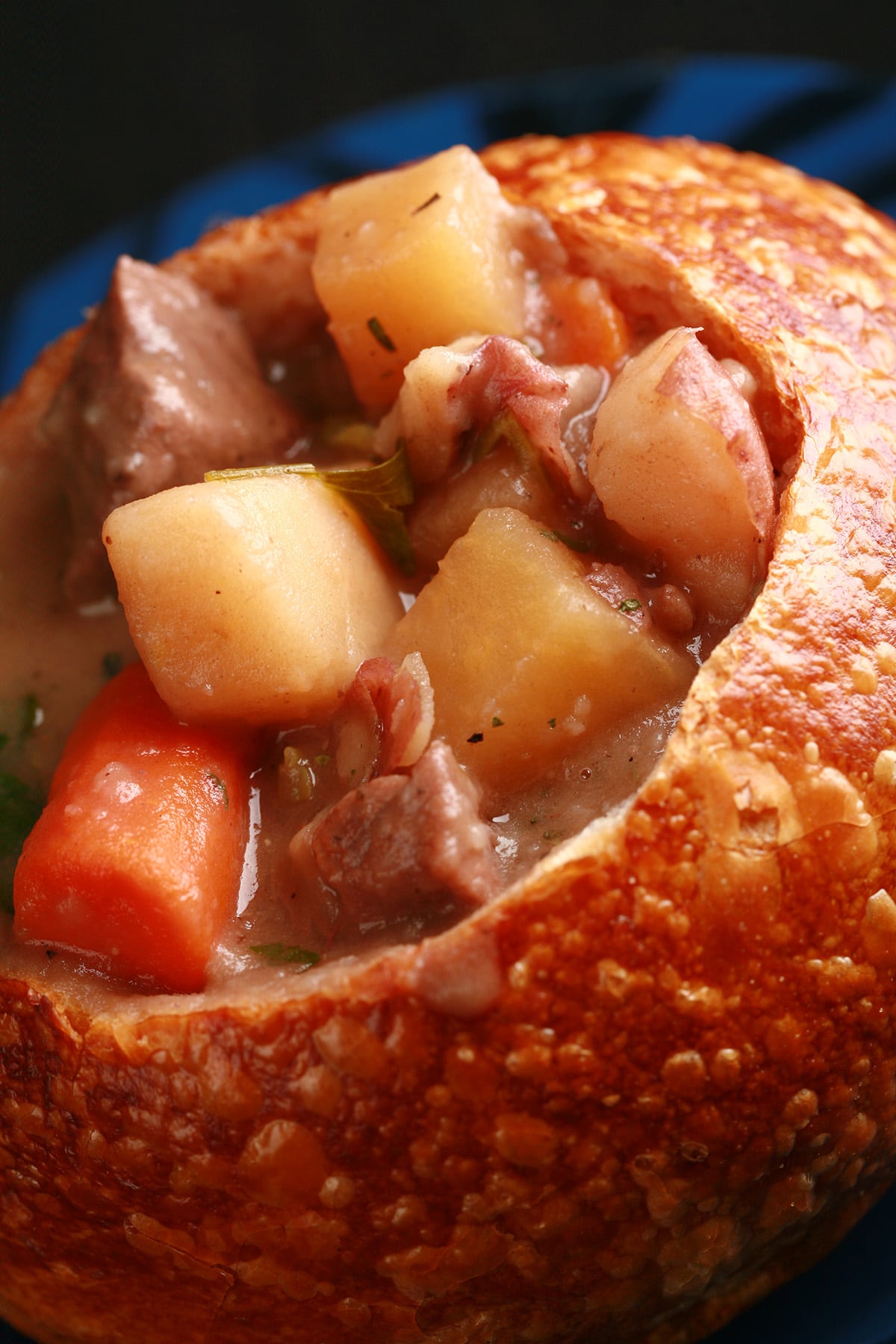 A bread bowl full of hearty beef stew. Chunks of beef, carrots, and potatoes are prominent.