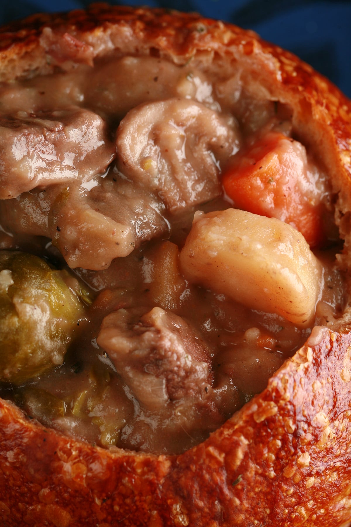 A bread bowl full of hearty beef stew. Chunks of beef, carrots, and potatoes are prominent.