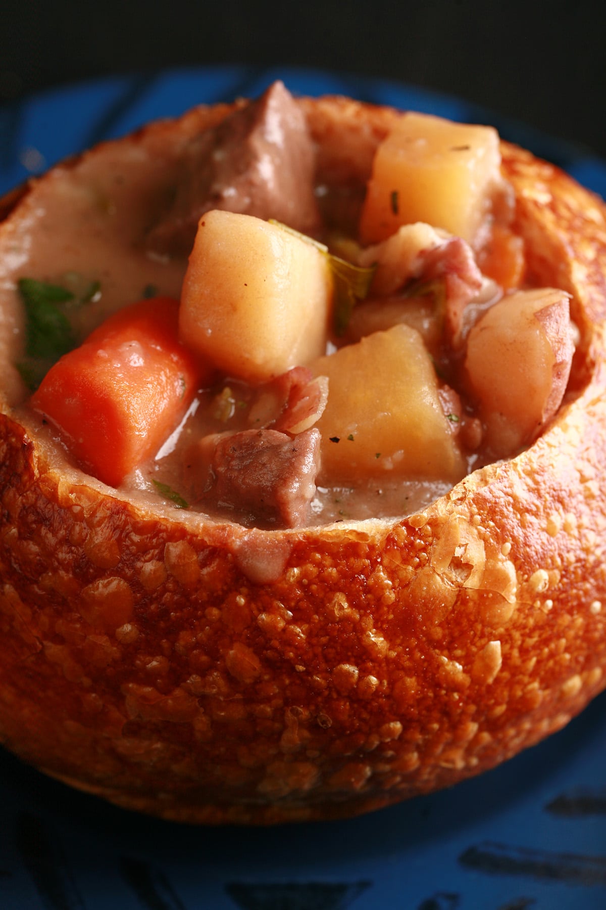 A bread bowl full of hearty beef stew. Chunks of beef, carrots, and potatoes are prominent.