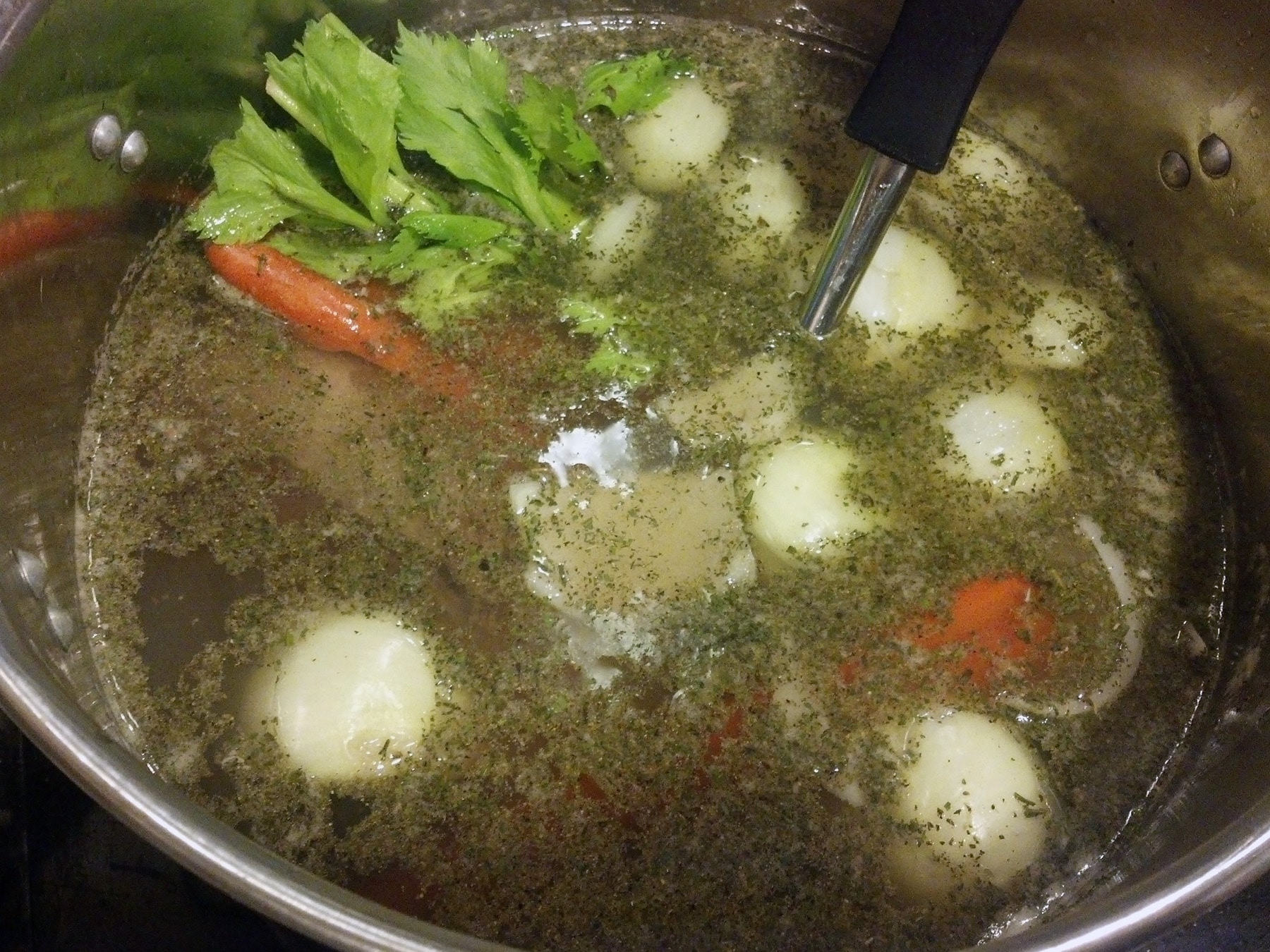 A large pot of seasoned water, simmering. Carrots, onion, celery, and herbs are visible.