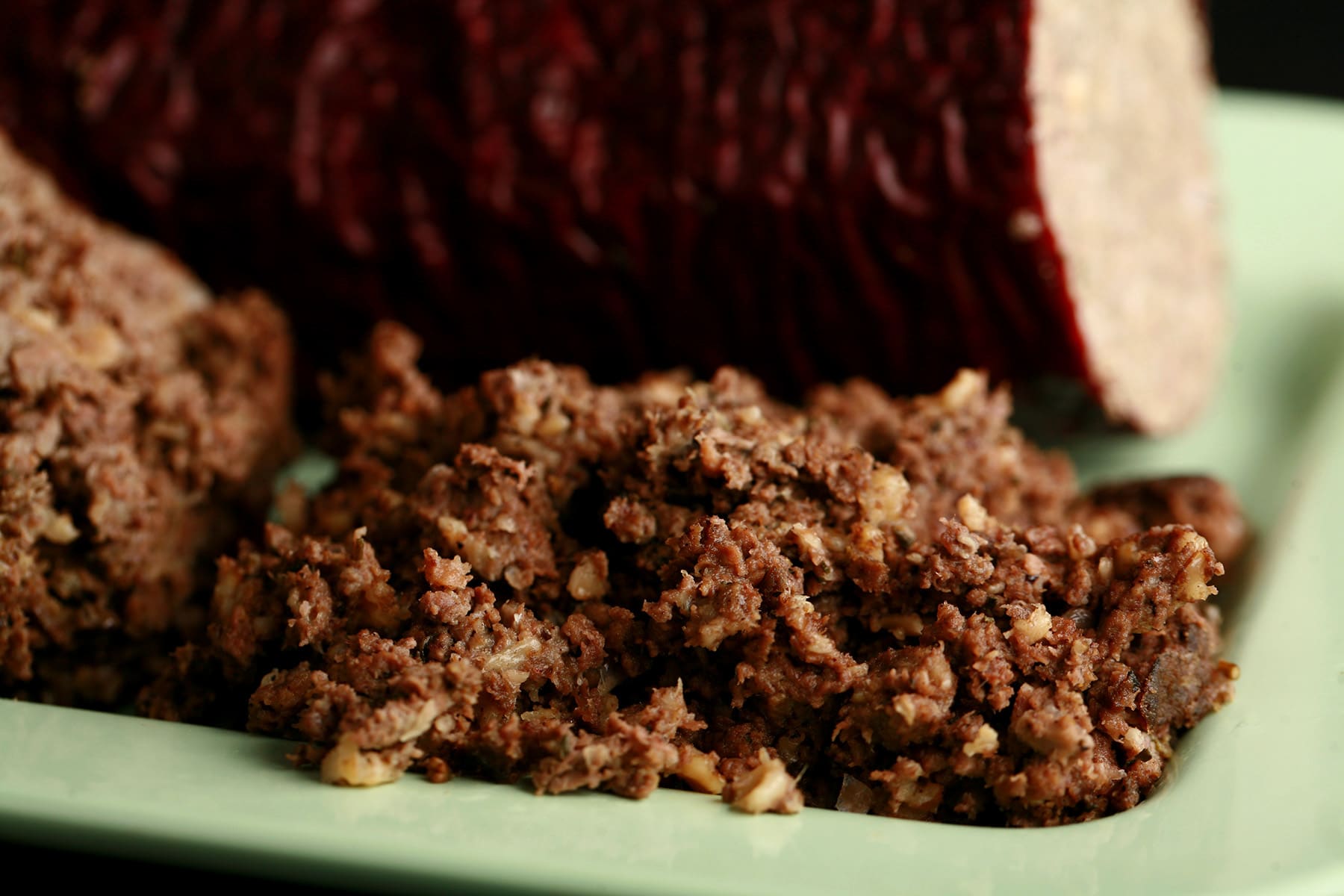 A green plate with a log of haggis "sausage", along with some loose haggis next to it.