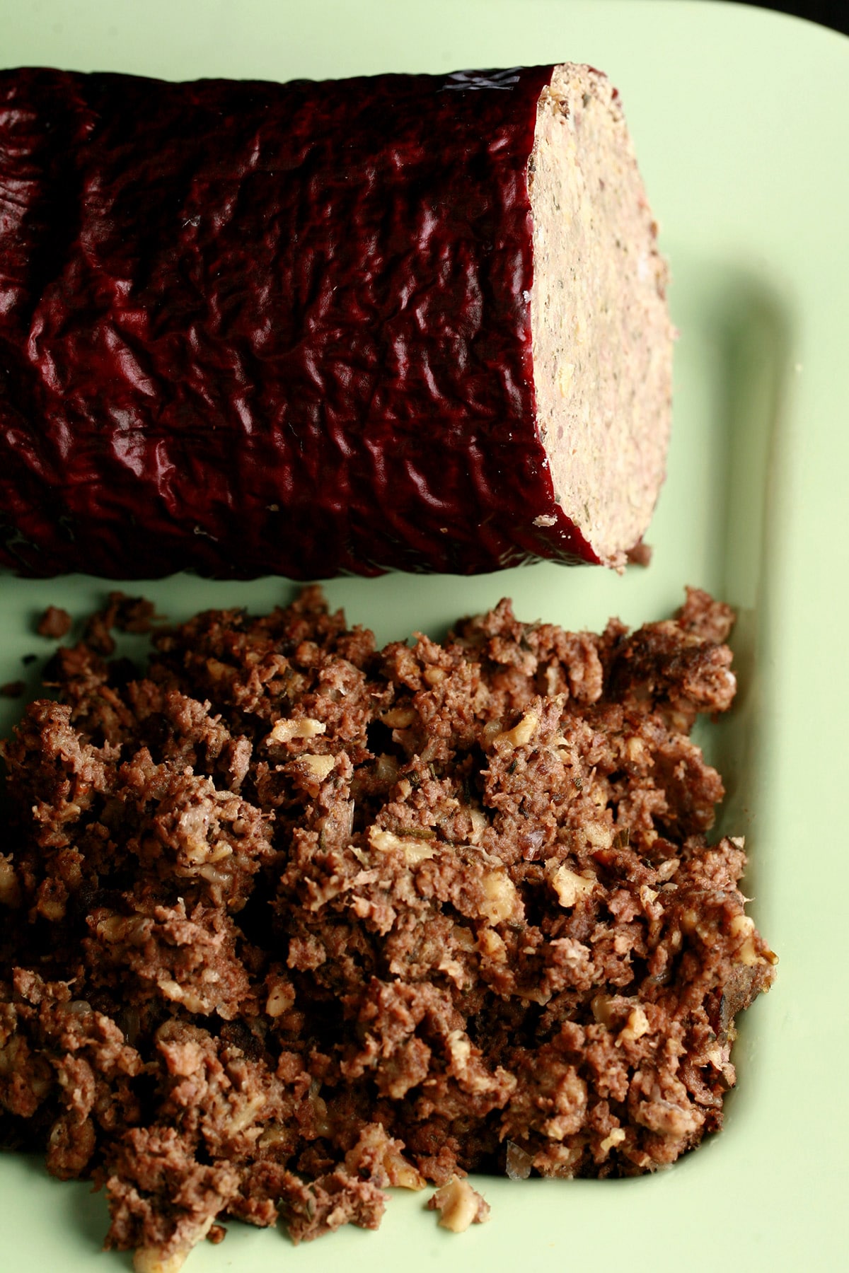 A green plate with a log of haggis "sausage", along with some loose haggis next to it.